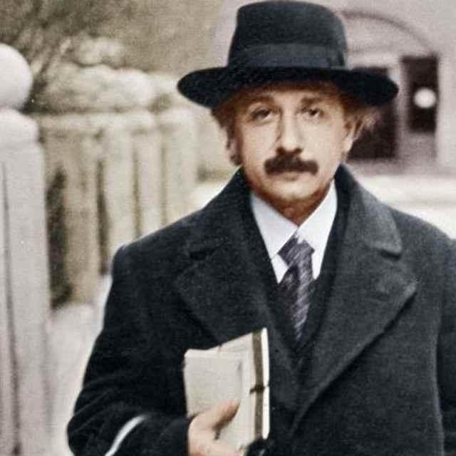 Young scientist Albert Einstein outside on a city street in a topcoat and hat