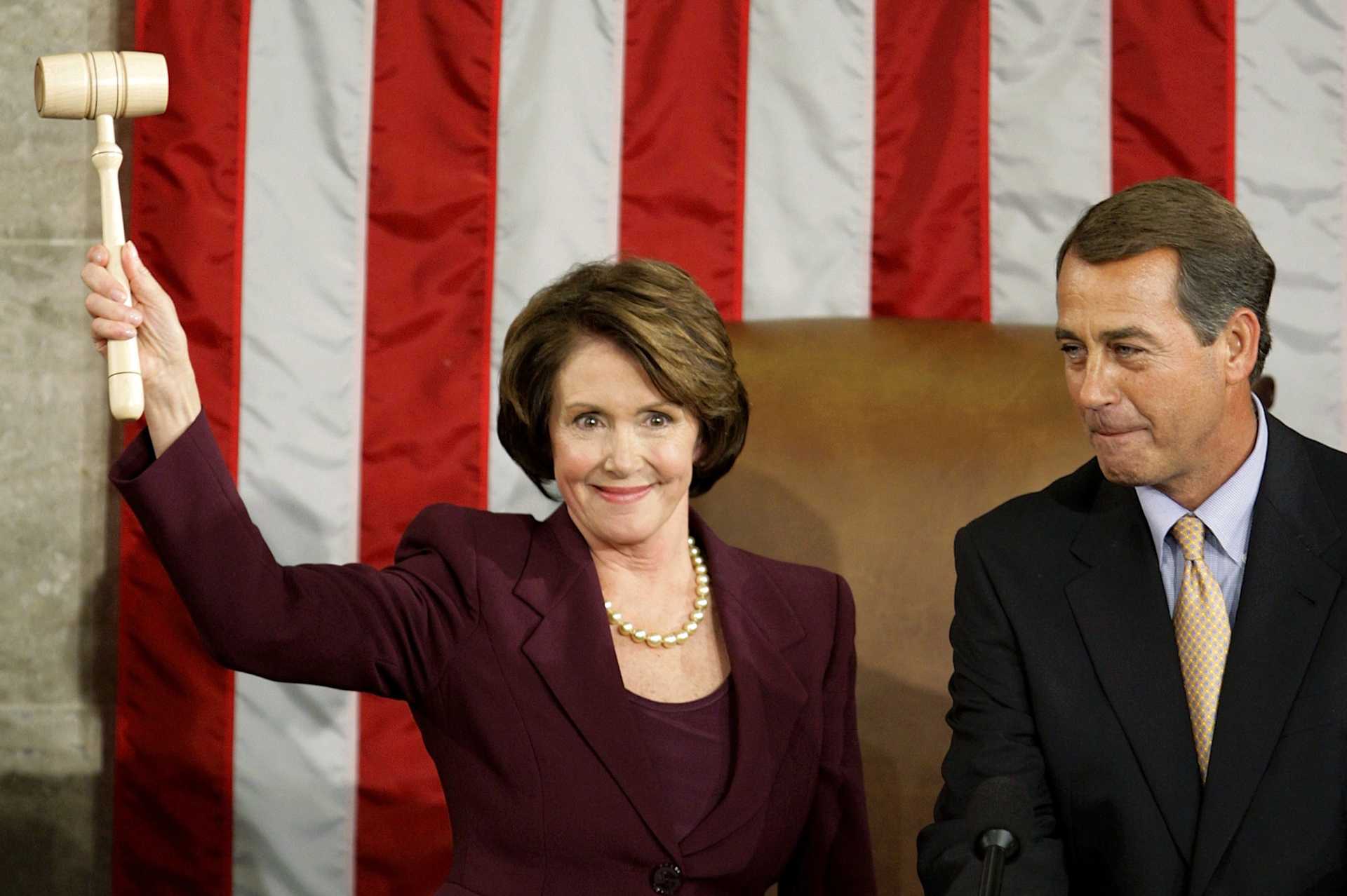A woman holds up a gavel as she and a man to the right stand in front of a large U.S. flag