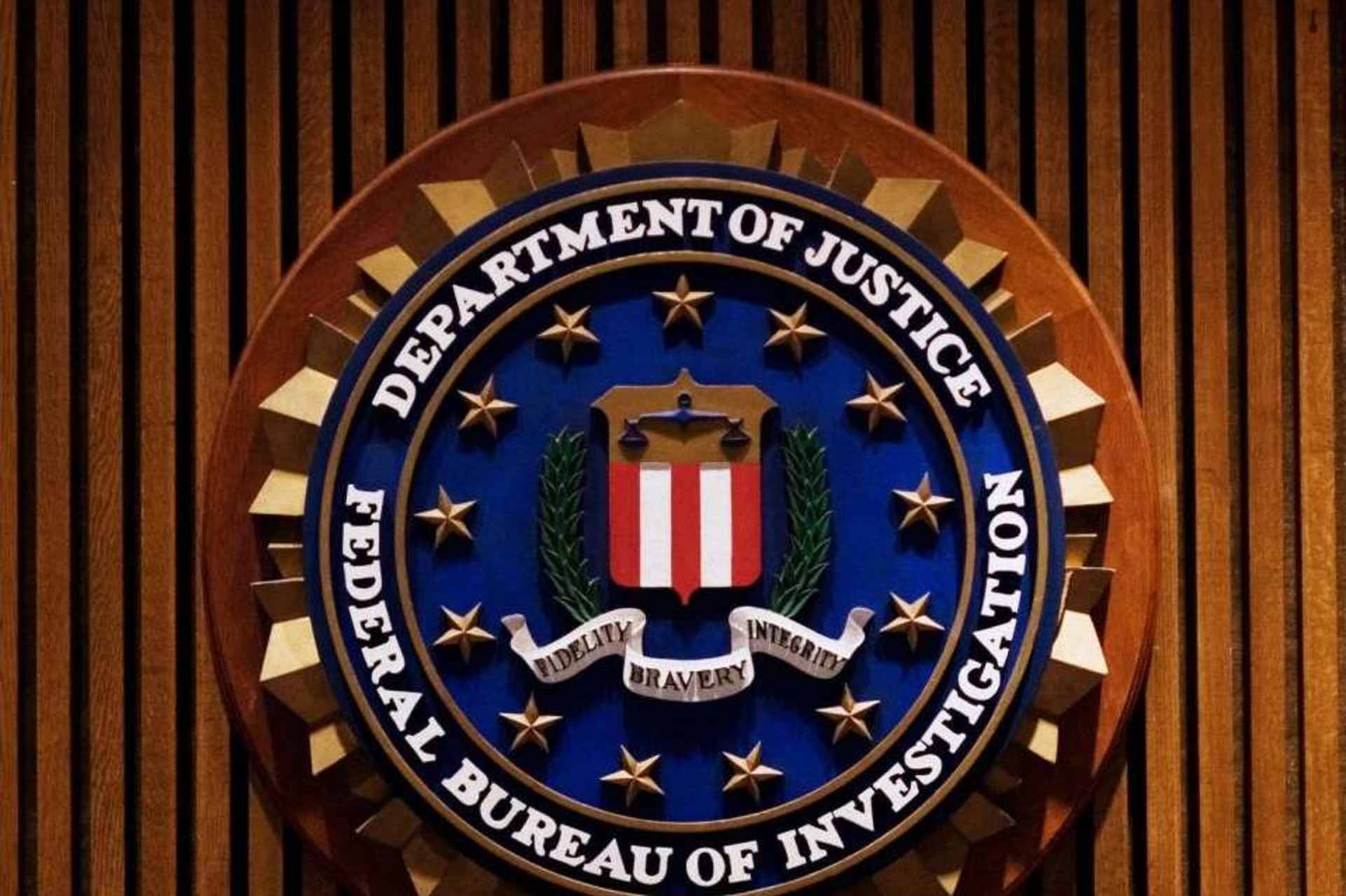 A wooden plaque with the seal of the United States Federal Bureau of Investigation (FBI) is displayed against a backdrop of wooden paneling.