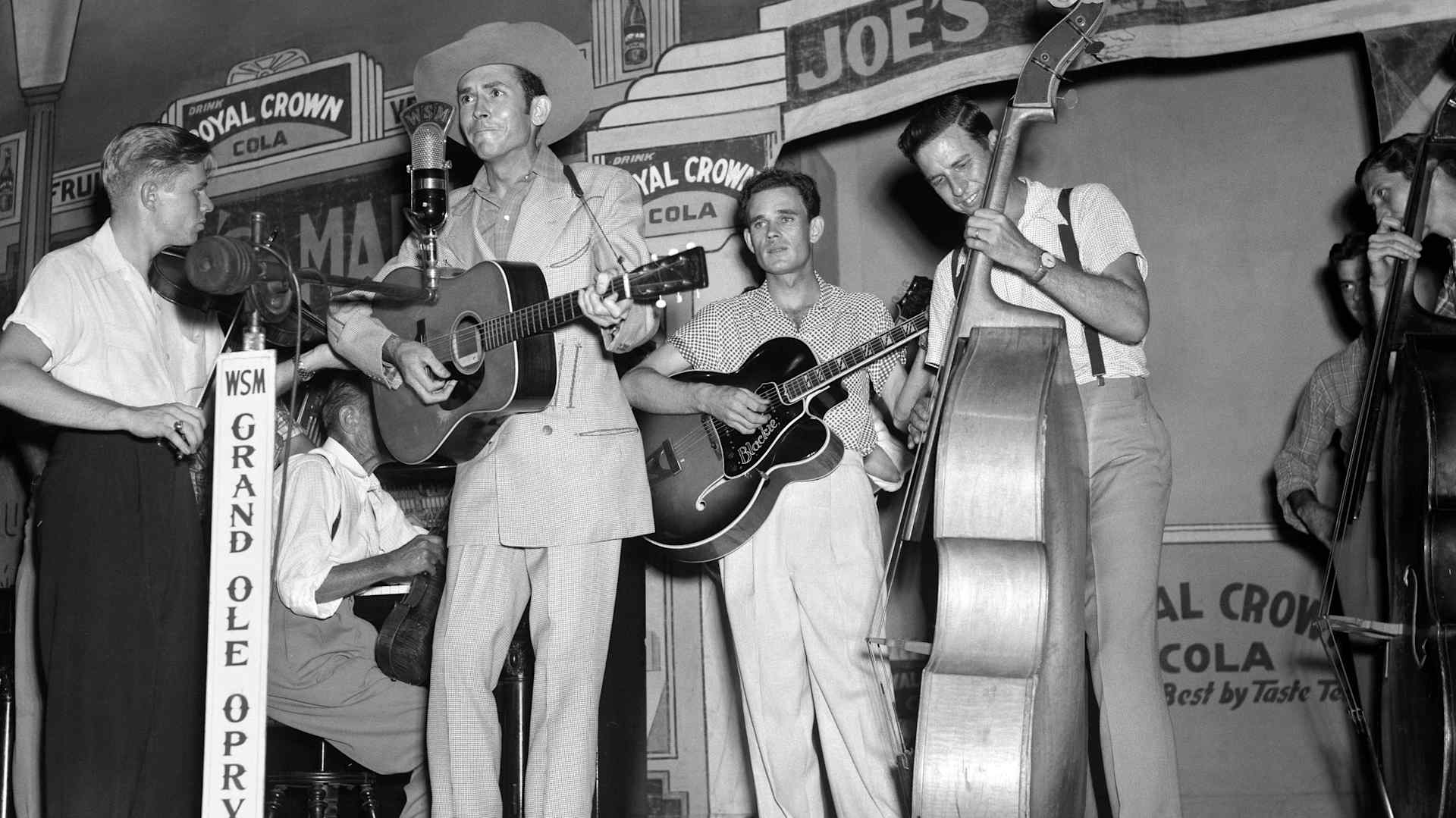 Country singer-songwriter Hank Williams performs with the Drifting Cowboys (Jerry Rivers on fiddle, Sammy Pruett on electric guitar, Howard Watts on bass) on stage at the Grand Ole Opry in one of his later performances, in 1951.