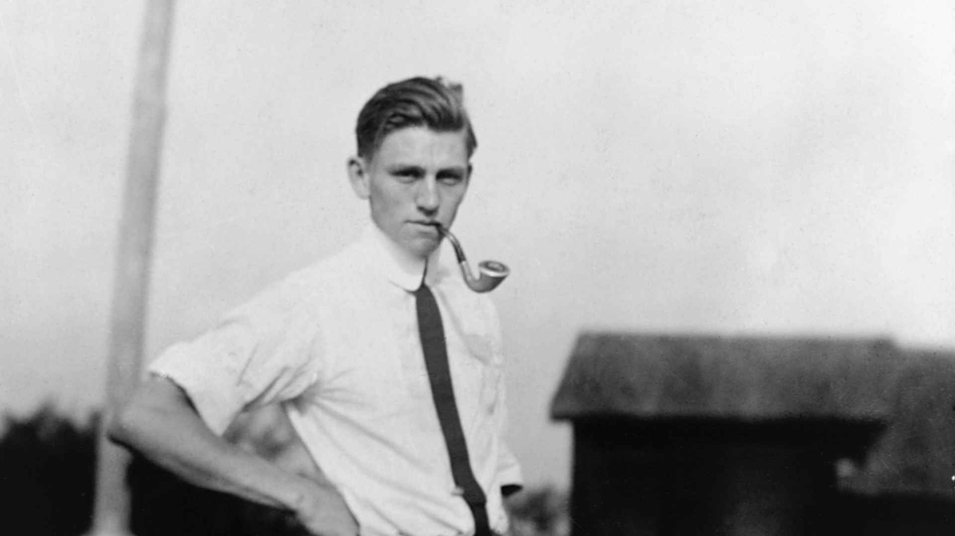 Gerald R. Ford, Sr., the stepfather of President Gerald R. Ford, Jr., standing in white shirtsleeves rolled up with a tie and pipe in his mouth