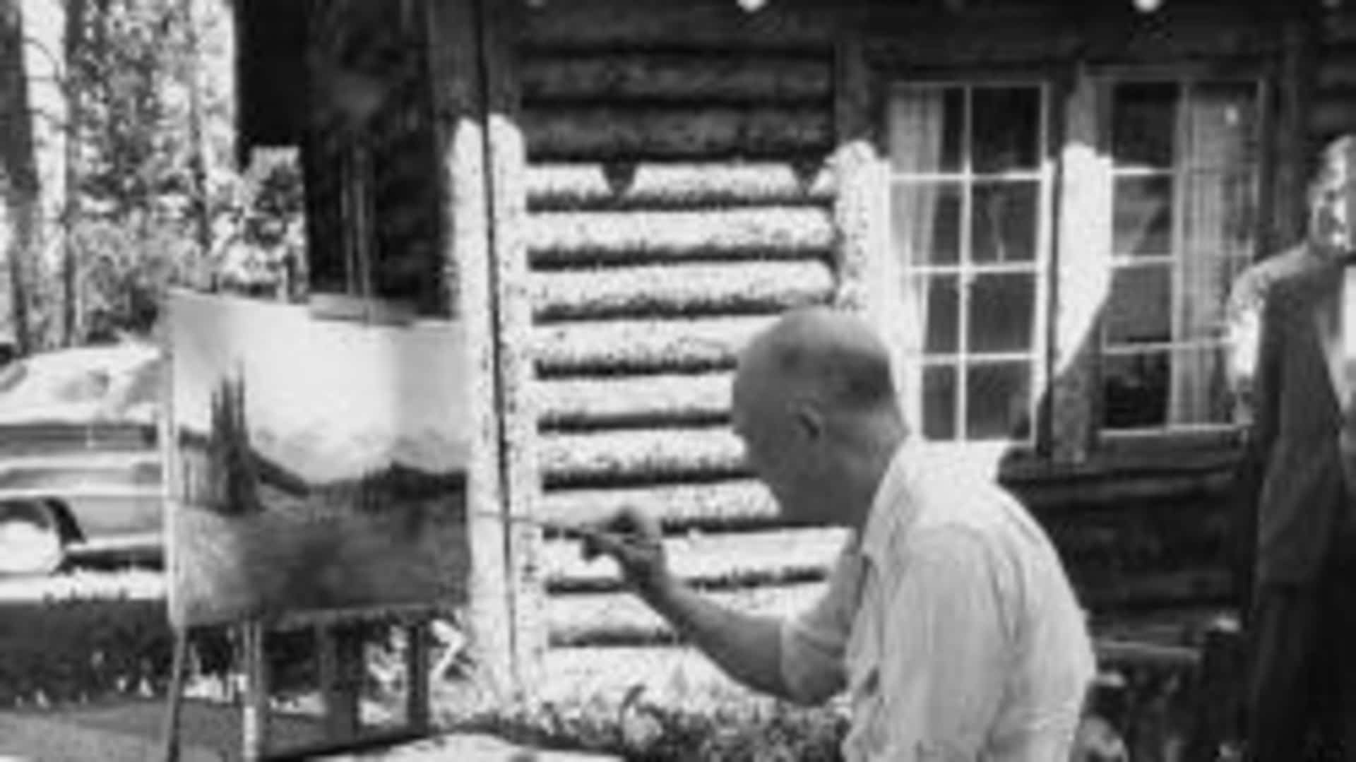 Eisenhower with his sleeves rolled up sitting in front of an easel with a paintbrush in his hand