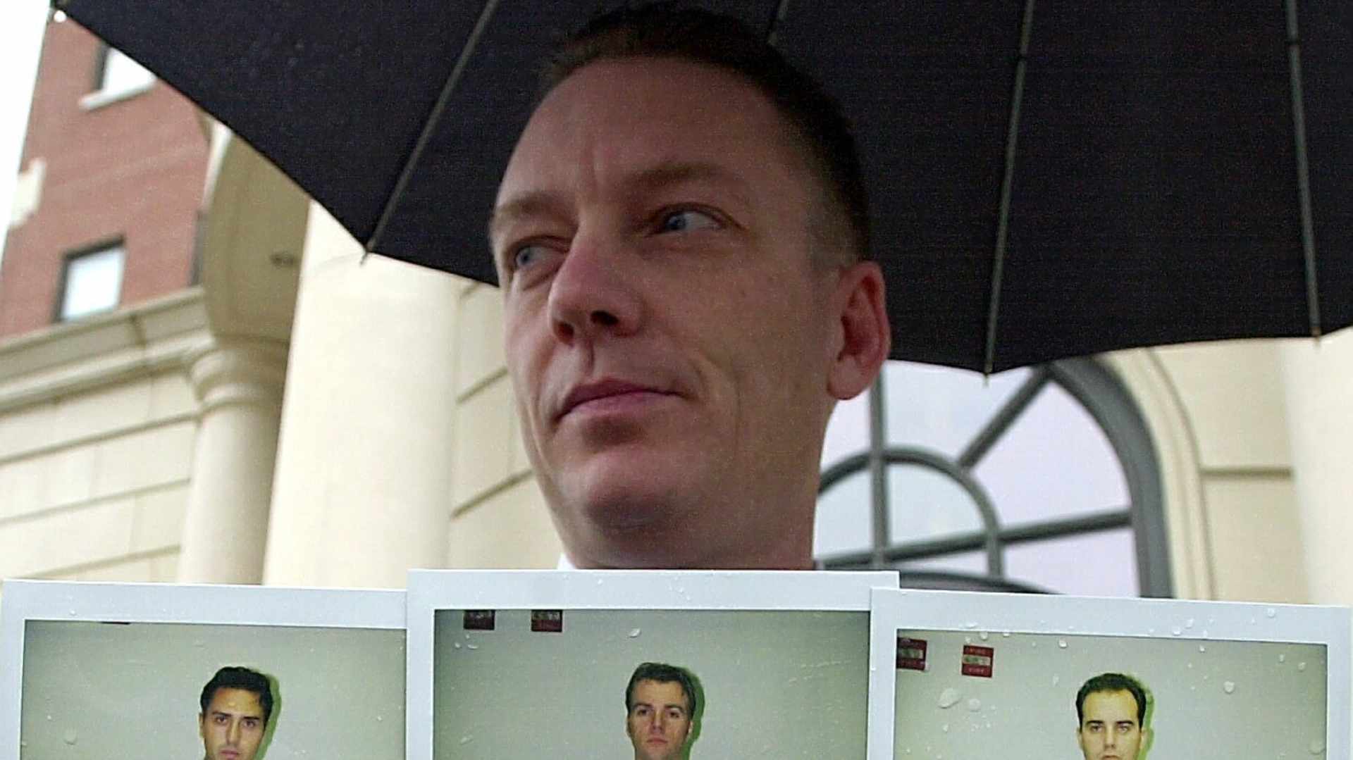 Lt. Robert Patnaude of the New York State Police Special Investigation Unit holds mugshots of Glen DaSilva, Derrick Davis and Christopher Harn outside the Federal Courthouse in White Plains, New York on November 12, 2002