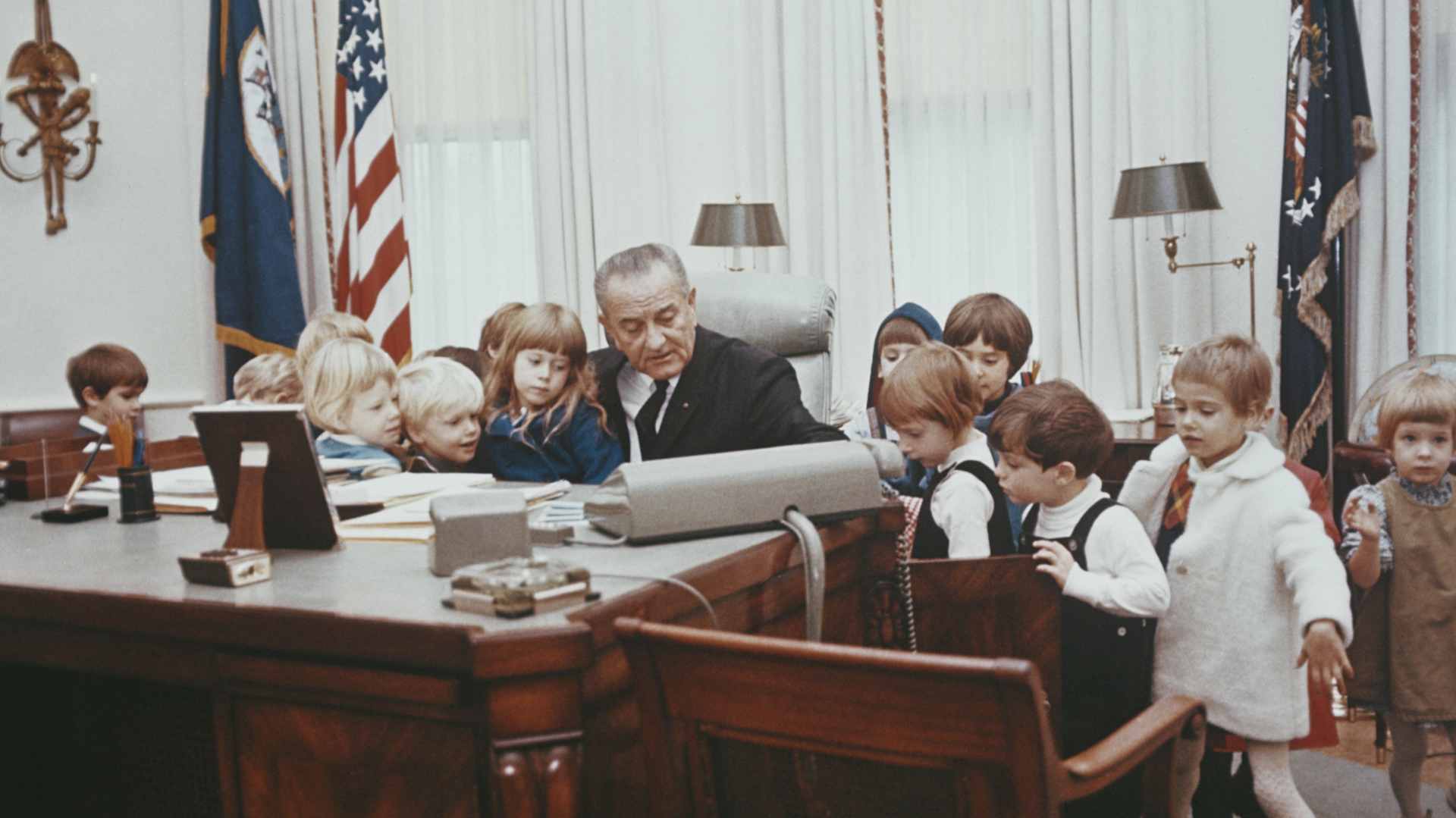 President of the United States, Lyndon B Johnson (1908-1973) pictured sitting at the Johnson desk as he gives a group of young children a tour of the Oval Office in the White House in Washington DC, circa 1967.