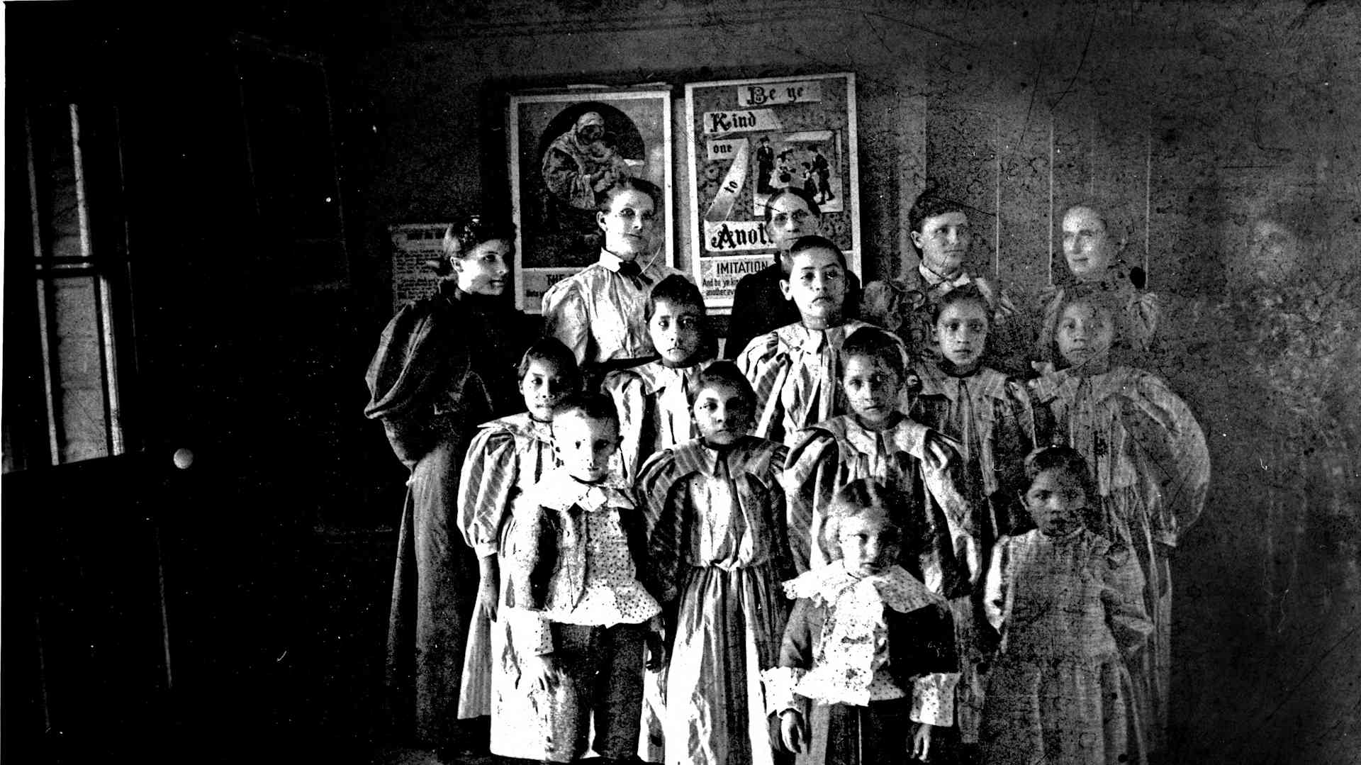A group of people, mostly children, standing together in a dimly lit room with various items and artwork displayed on the walls behind them.