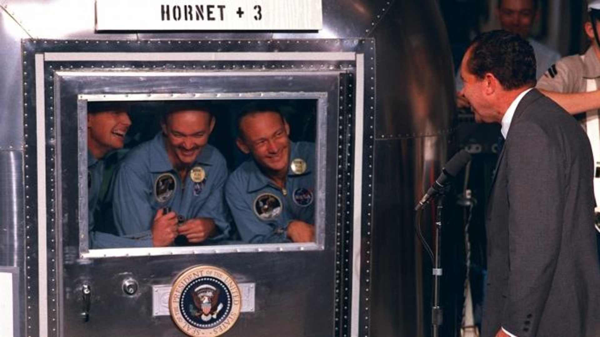President Richard M. Nixon was in the central Pacific recovery area to welcome the Apollo 11 astronauts. Already confined to the Mobile Quarantine Facility (MQF) are (left to right) Neil A. Armstrong, commander; Michael Collins, command module pilot; and Edwin E. ("Buzz") Aldrin Jr., lunar module pilot. (Credit: NASA)