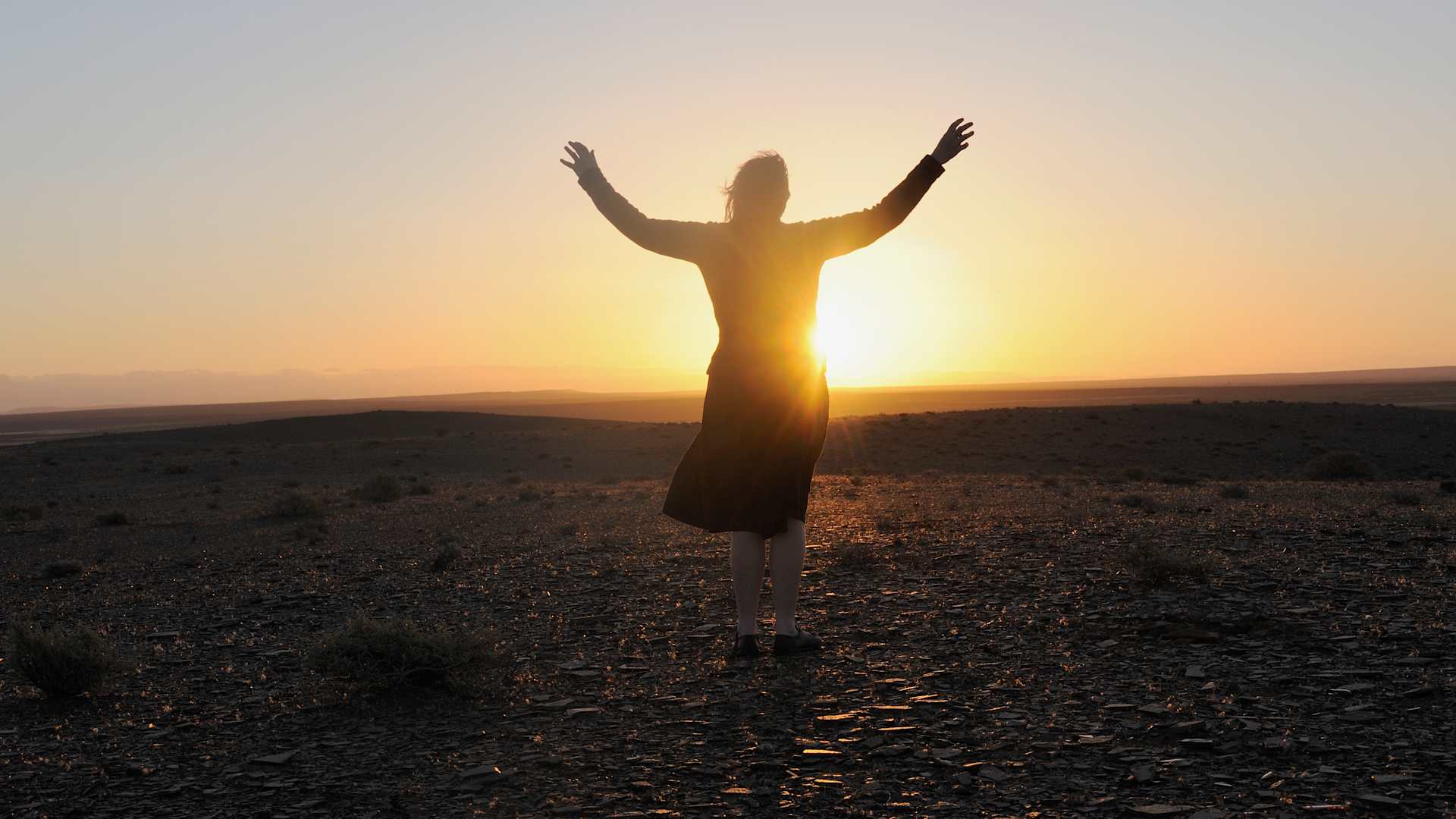Woman with outstretched arms facing sun.