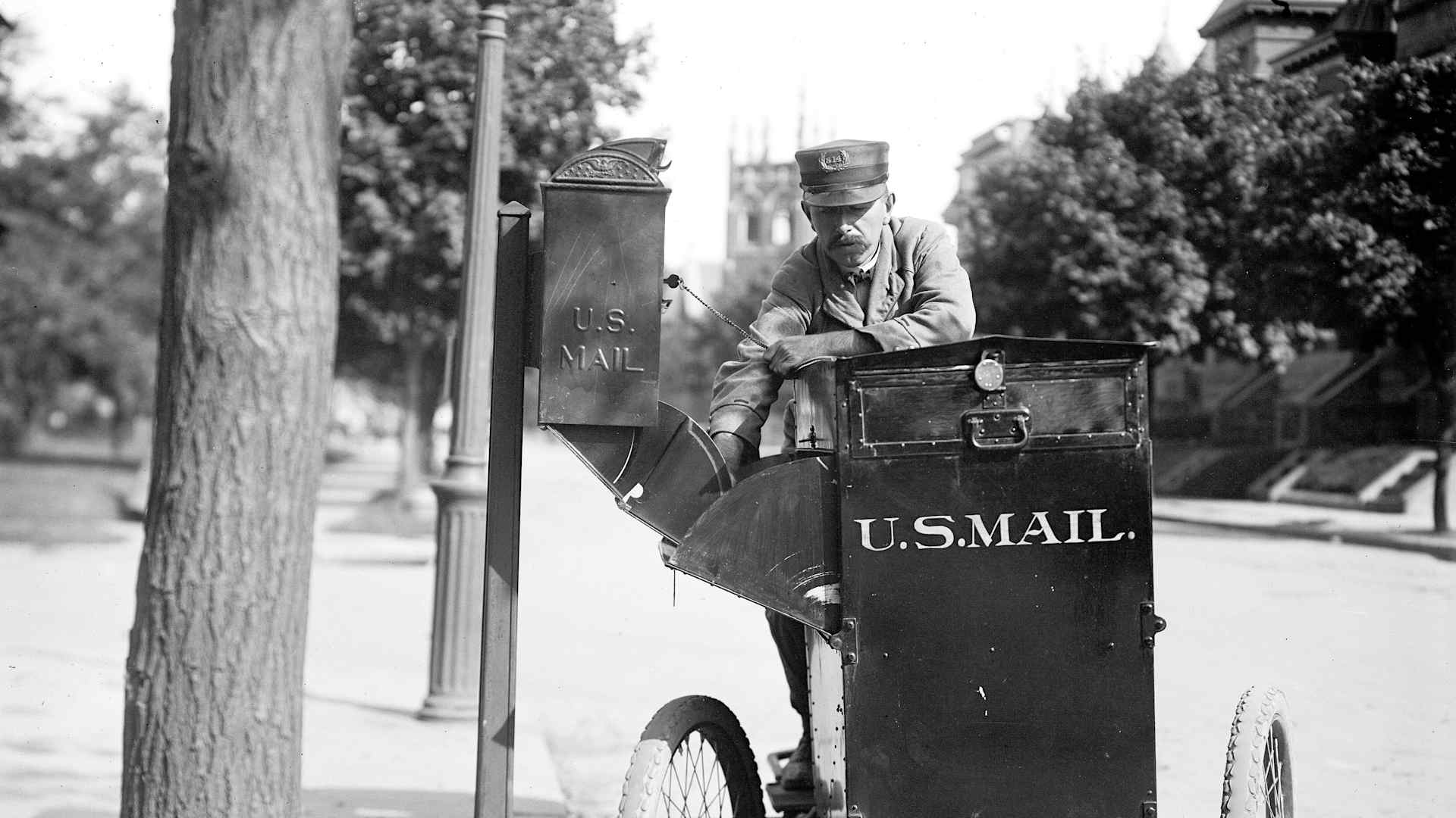 Historical United States Postal Service: Mailman on a motorcycle picking up mail from a box circa 1912