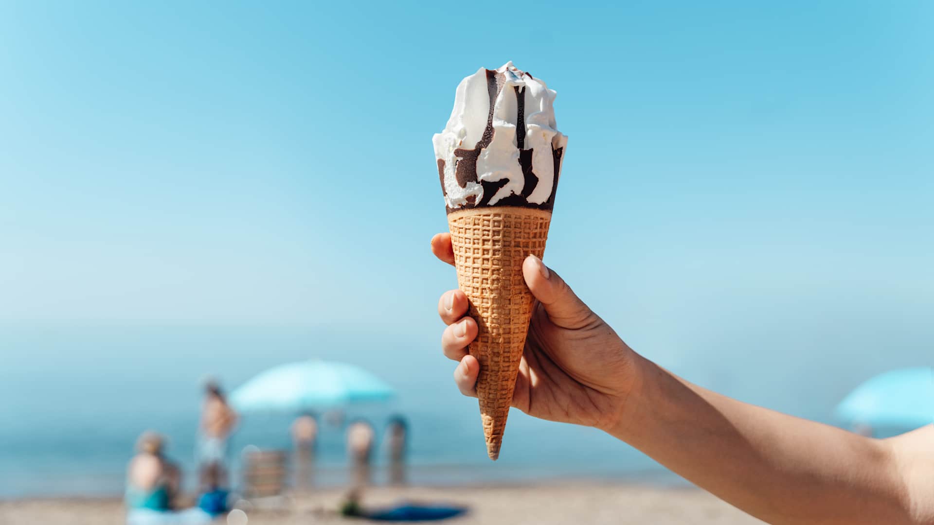 Female hand holding ice-cream on the beach against clear blue sky
