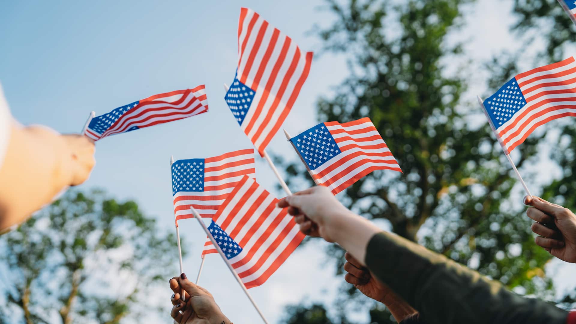A group of people is waving small American flags at sunset