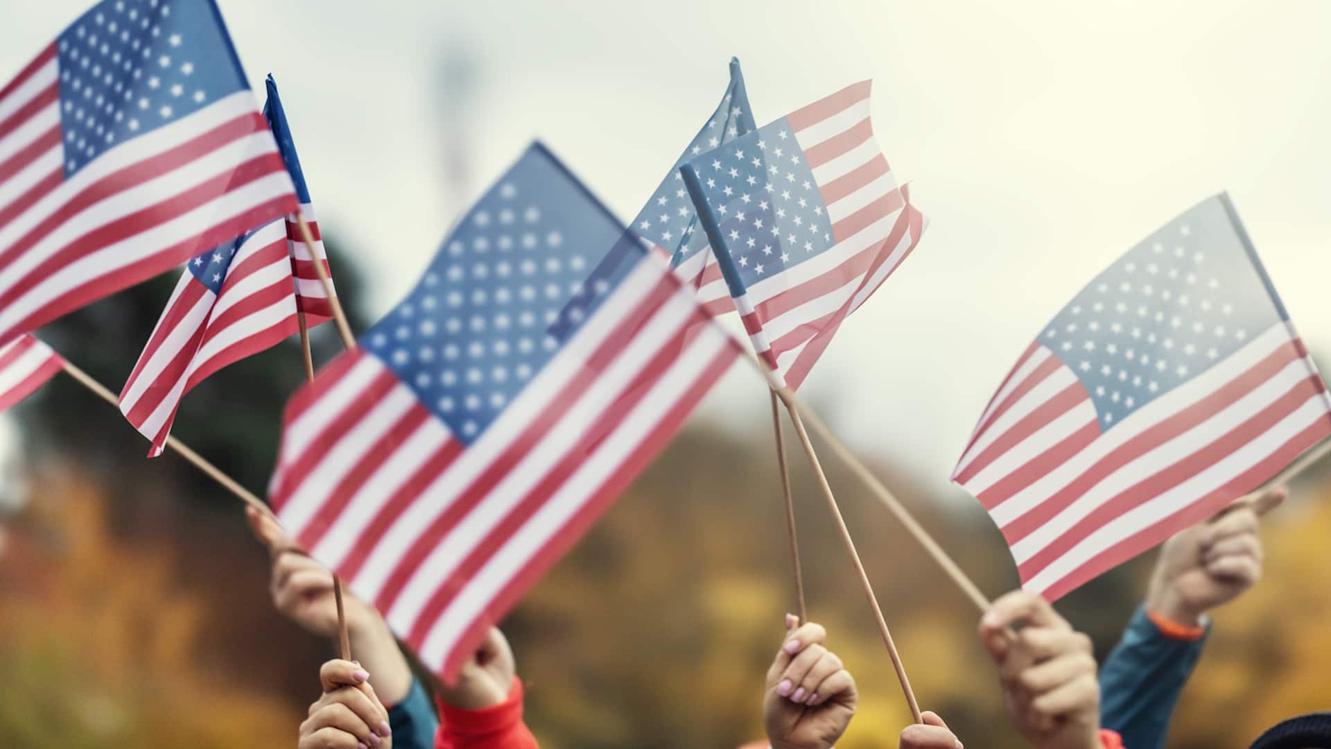 Group of people waving small American flags at sunset. Concept for different topics like Election Results, Happy Veterans Day, Labor Day, Independence Day, President day.