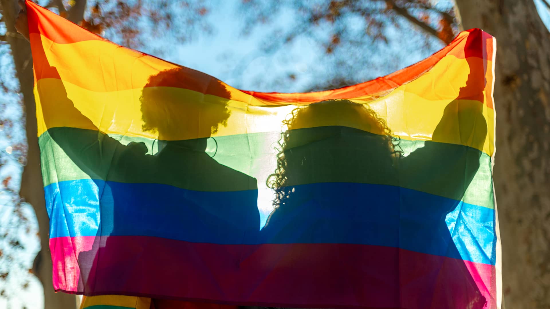 Two people holding a lgbt flag behind their backs
