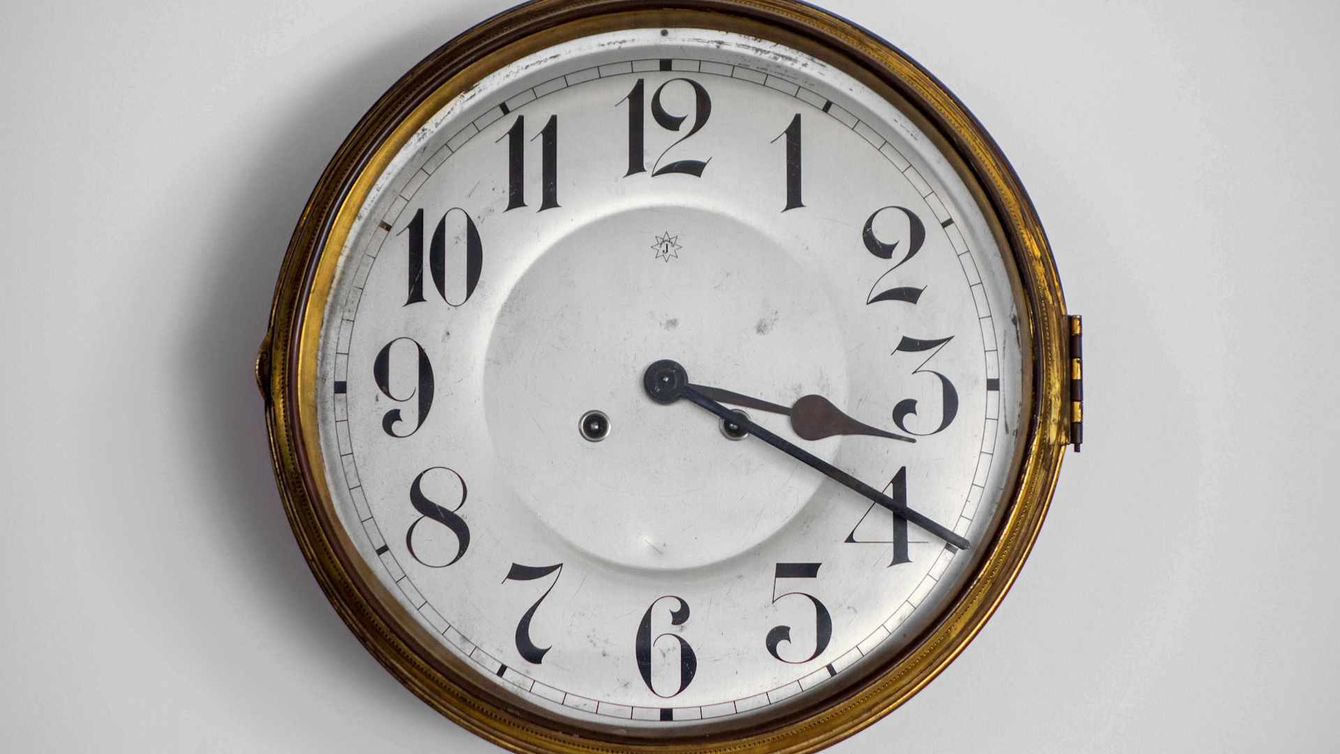 An antique oval-shaped wall clock with a wooden frame and a white dial displaying the time.