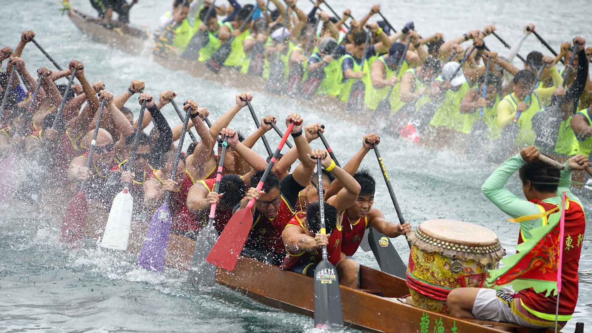 Participants compete in a dragon boat race, jammed into a long skinny boat, rowing while a drummer pounds out the beat