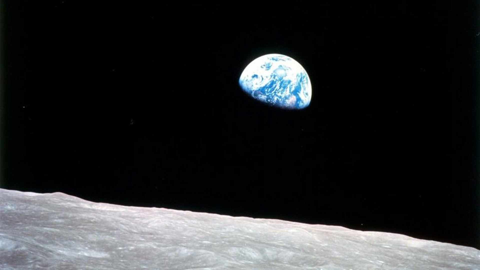 Blue-and-white orb of the earth in the vast blackness of space hanging over the crater-pocked surface of the moon