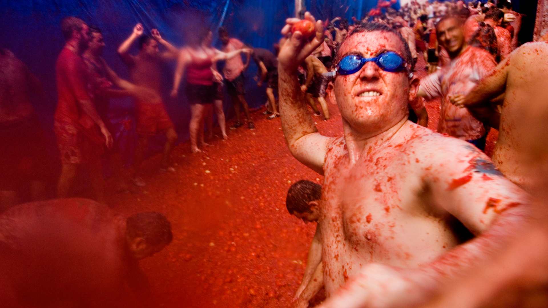 Man wearing swimming goggles throwing a tomato at La tomatina food fighting festival. Bunol. Valencia Spain