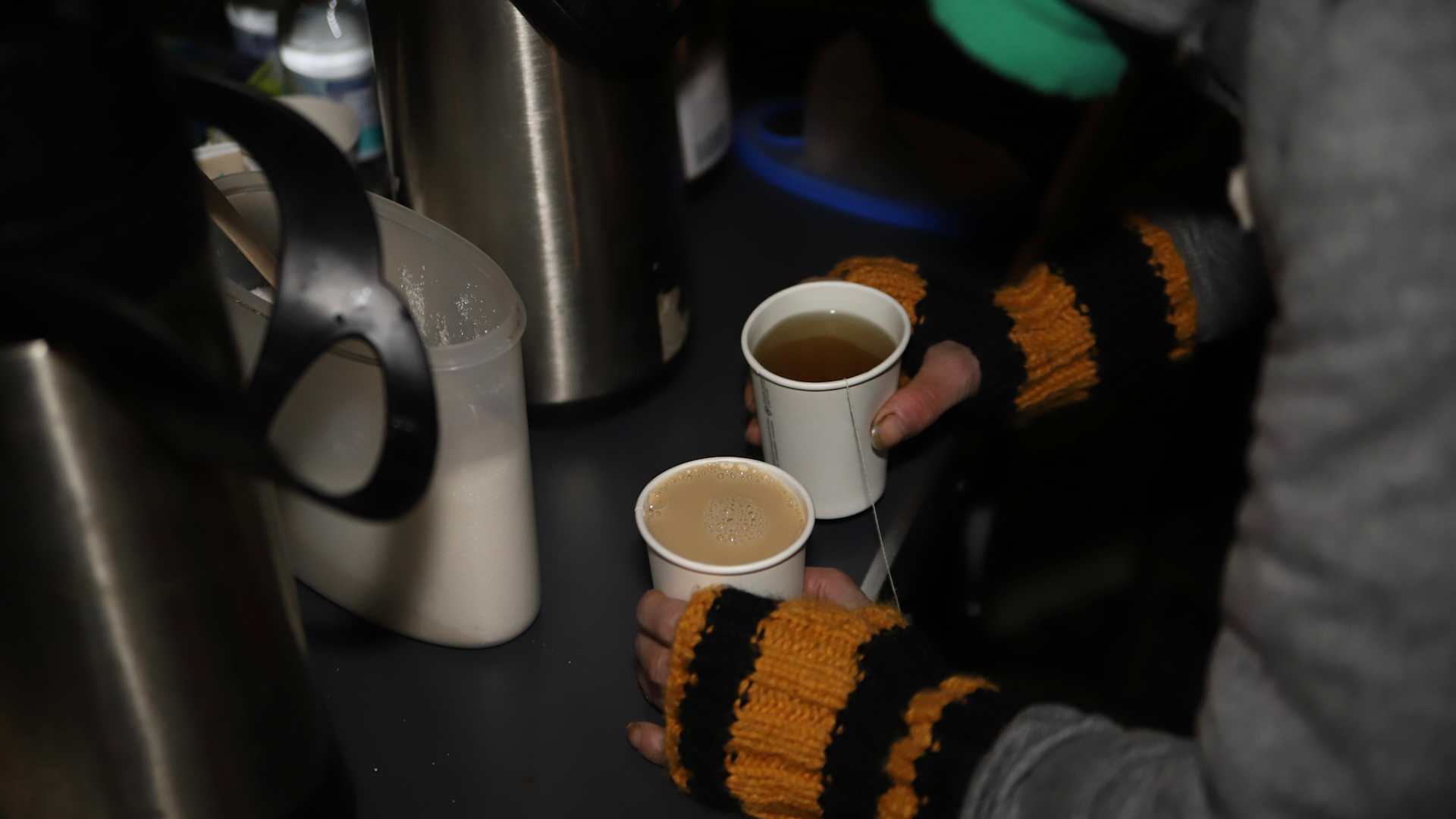 A needy person takes tea and coffee from a table in paper cups.
