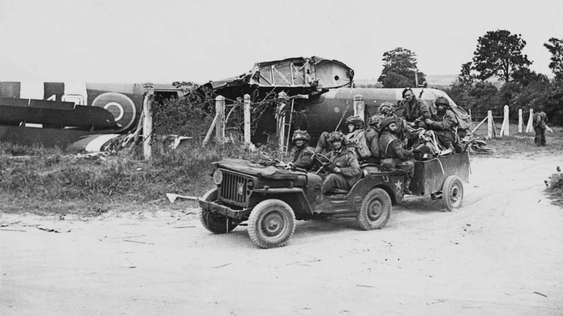 Hiram Clough (driving Jeep), Lance Corporal Joe Wilkenson and Kenneth Brierley (seated at the back of the Jeep) of the 716 (Airborne) Light Composite Company RASC (Royal Army Service Corps), British 6th Airborne Division in a Willys Jeep and trailer with glider pilots and other members of the unit following their landing from the damaged wooden Airspeed AS51 Horsa glider on a supply run on D-Day, 6th June 1944 at a landing ground near Ranville in Normandy, France.
