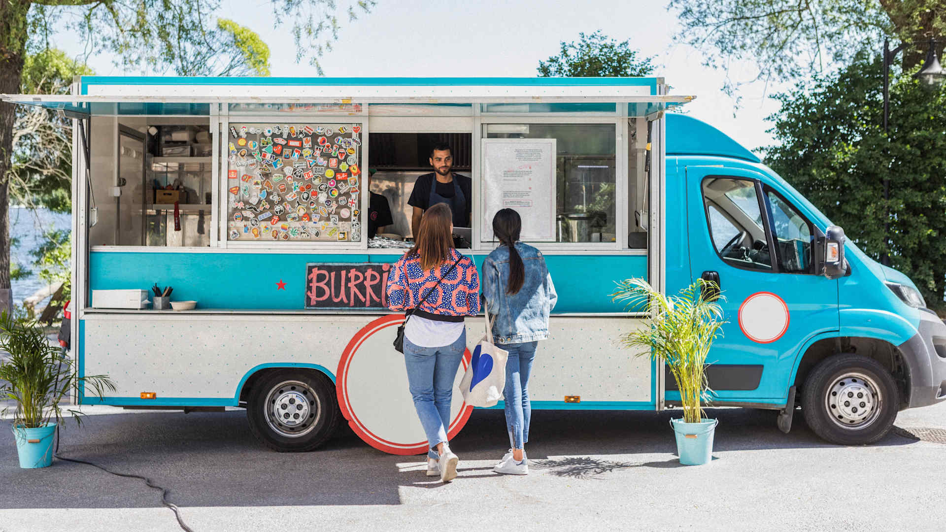 Full length rear view of female friends talking with male food truck owner in city on sunny day - stock photo