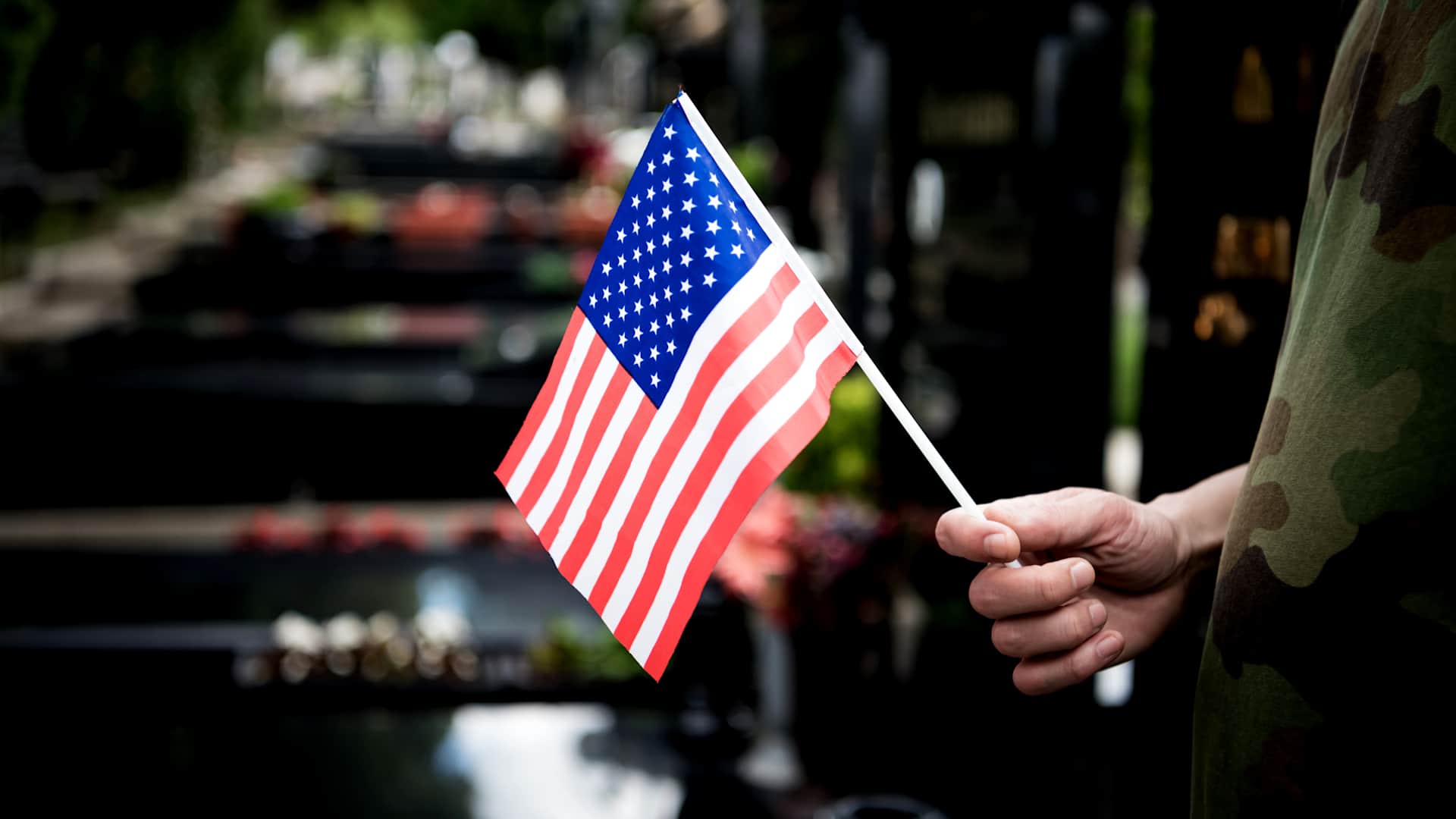 A soldier holds an American flag at a cemetery.