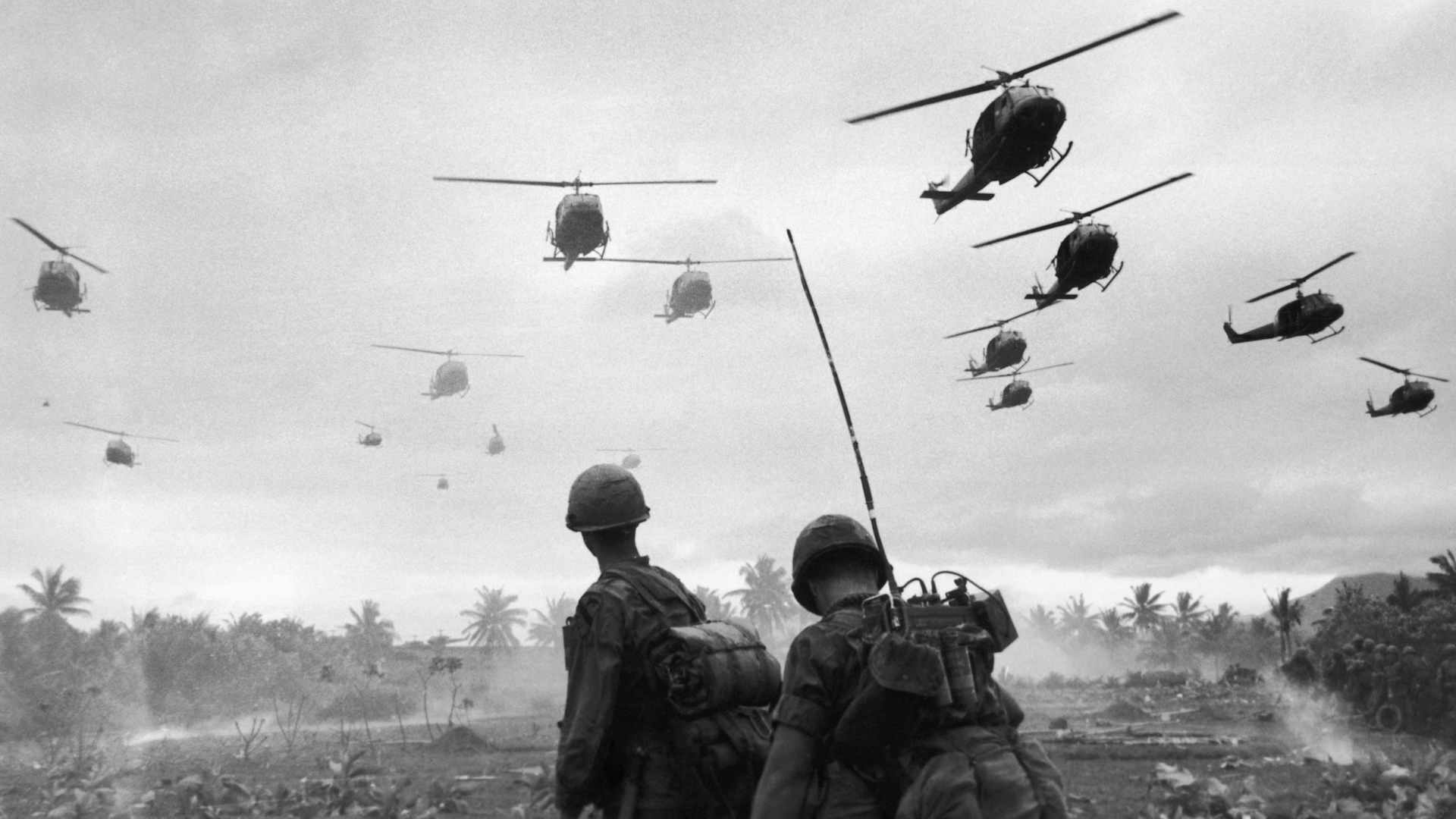 The second wave of combat helicopters of the 1st Air Cavalry Division fly over an RTO and his commander on an isolated landing zone during Operation Pershing, a search and destroy mission on the Bong Son Plain and An Lao Valley of South Vietnam, during the Vietnam War. The two American soldiers are waiting for the second wave to come in.
