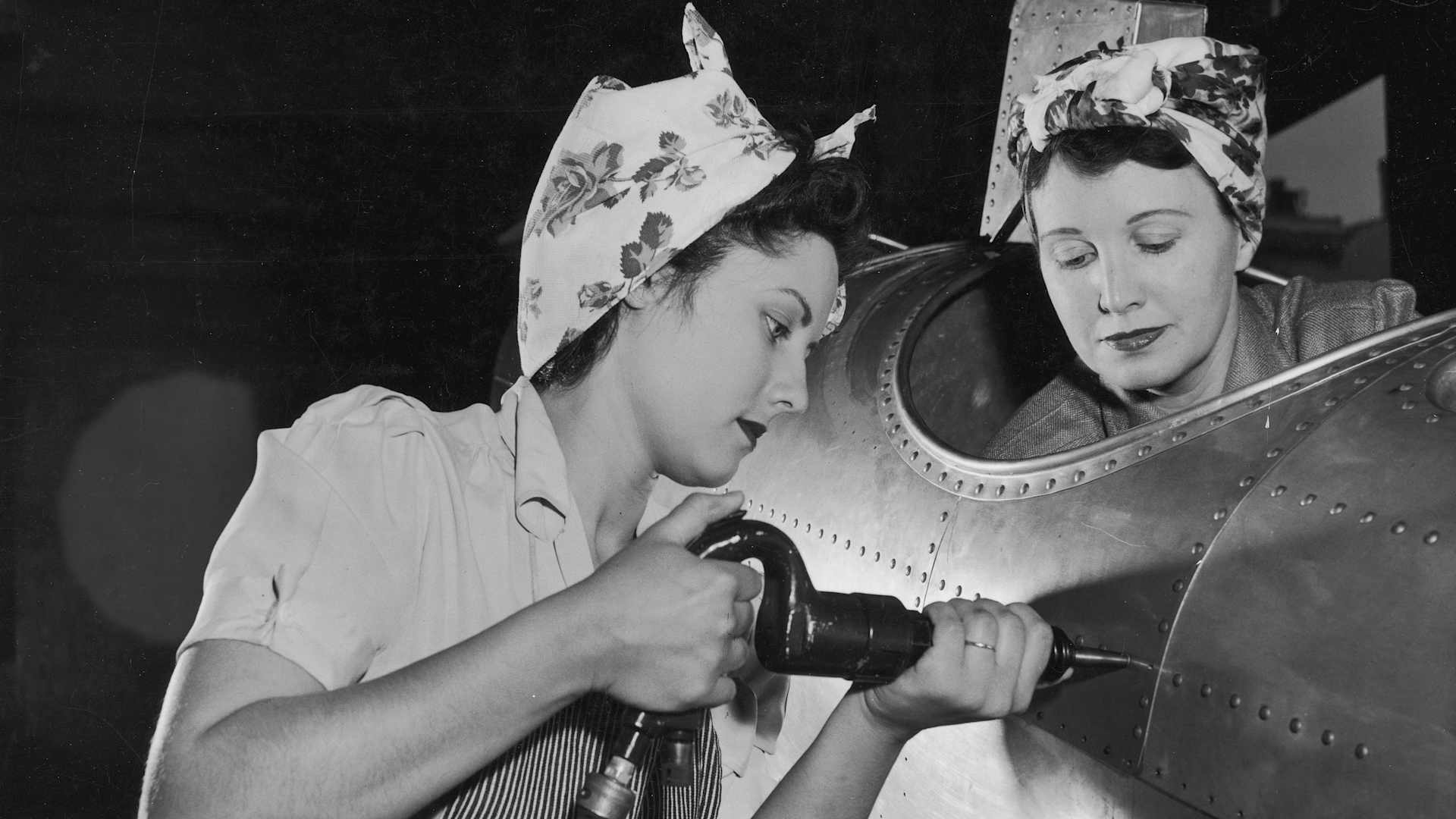 circa 1943: One American female worker drives rivets into an aircraft while another sits in the cockpit on the US home front during World War II. Women who went to work in industries to aid the war effort became known under the moniker 'Rosie the Riveter'.