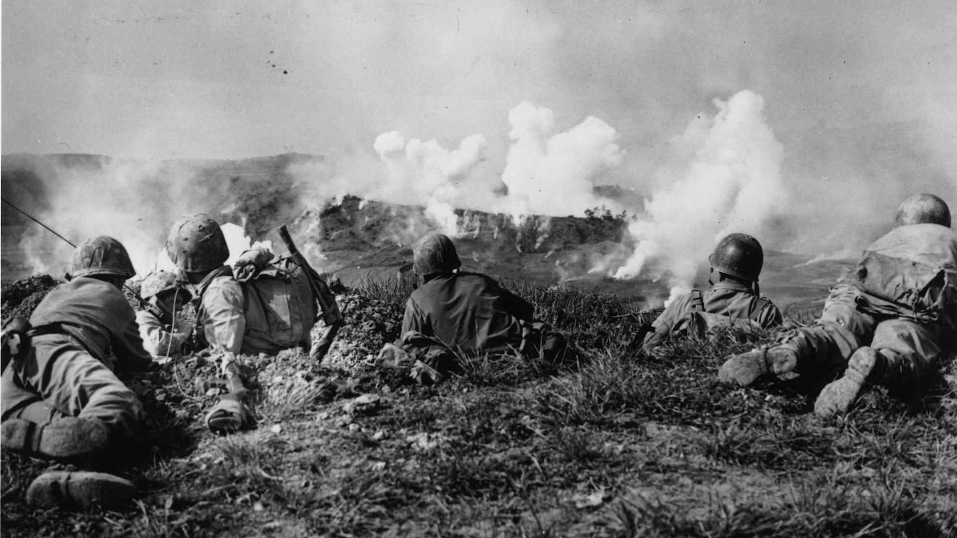 Battle of Okinawa: U.S. Marines of the 1st Division wait on the crest of a hill in southern Okinawa, as they watch phosphorous shells explode over Japanese soldiers dug into the hills.