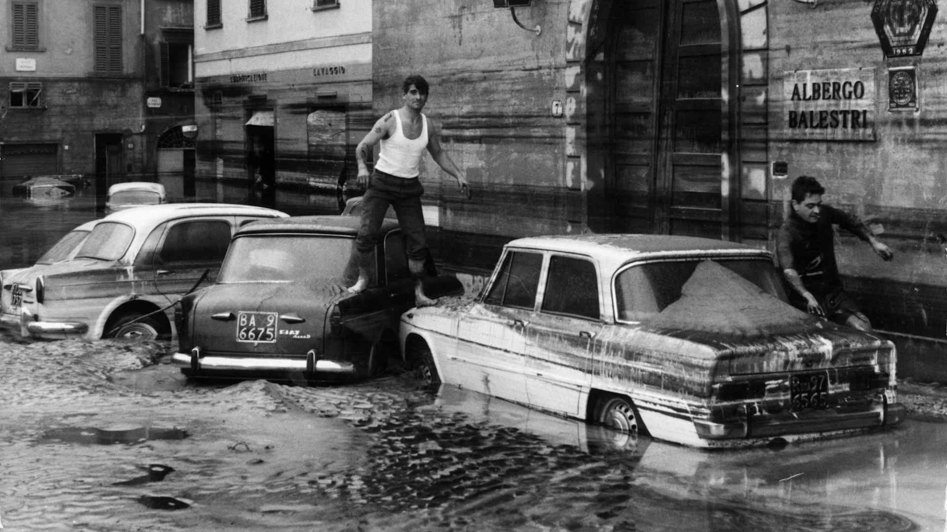 7th November 1966: Pedestrians use marooned cars as stepping stones in the flooded streets of Florence after the River Arno had burst its banks.