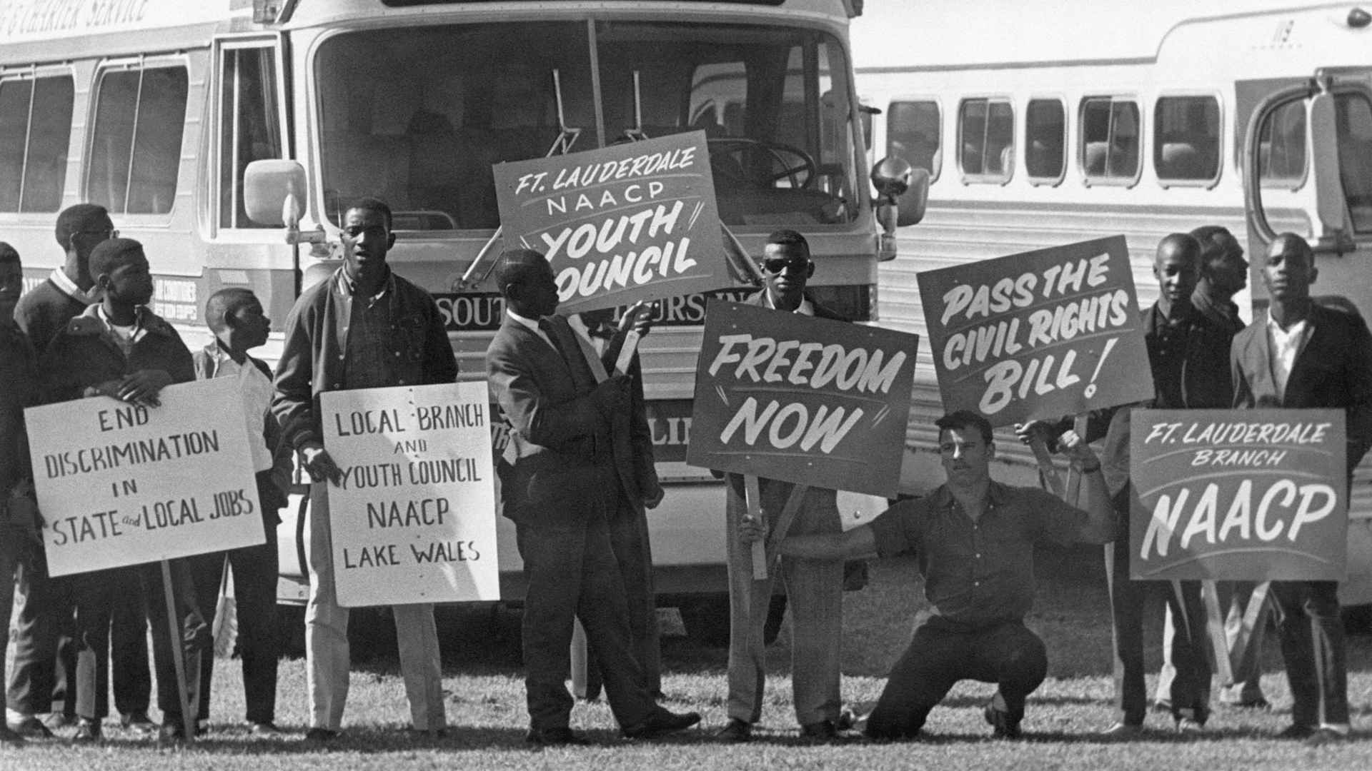 Marchers and members of the NAACP holding signs gather at a school athletic field in Tallahassee, Florida before a civil rights march.