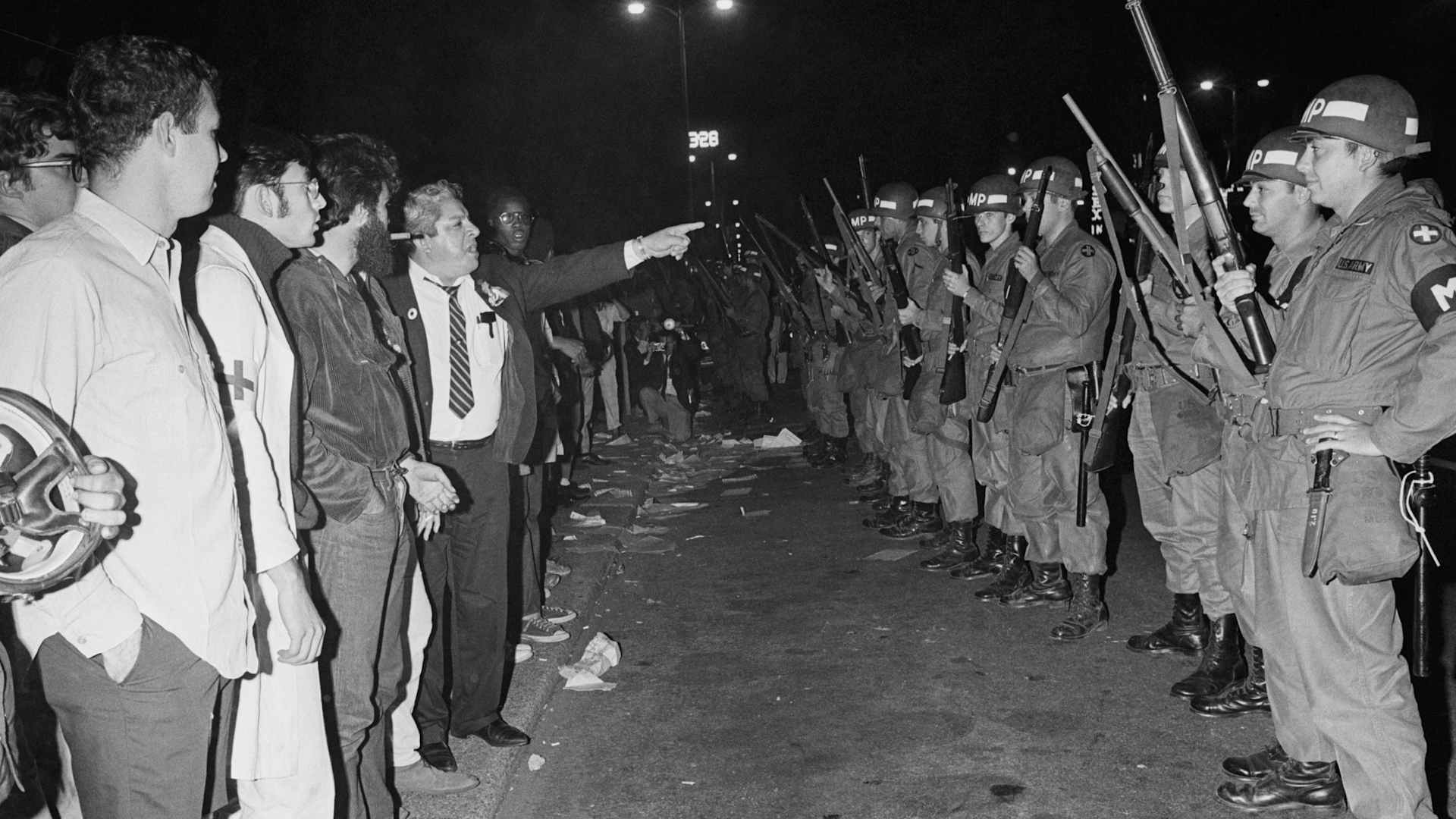 (Original Caption) Chicago, IL: An unidentified bystander points accusingly at Illinois National Guardsmen as they stand guard of Grant Park early 8/28 following a large scale confrontation with hippies. Seven hundred troops, all members of the 33rd MP battalion, were ordered into the park, across the street from Democratic National Convention Headquarters at the Conrad Hotel. 8/28/1968