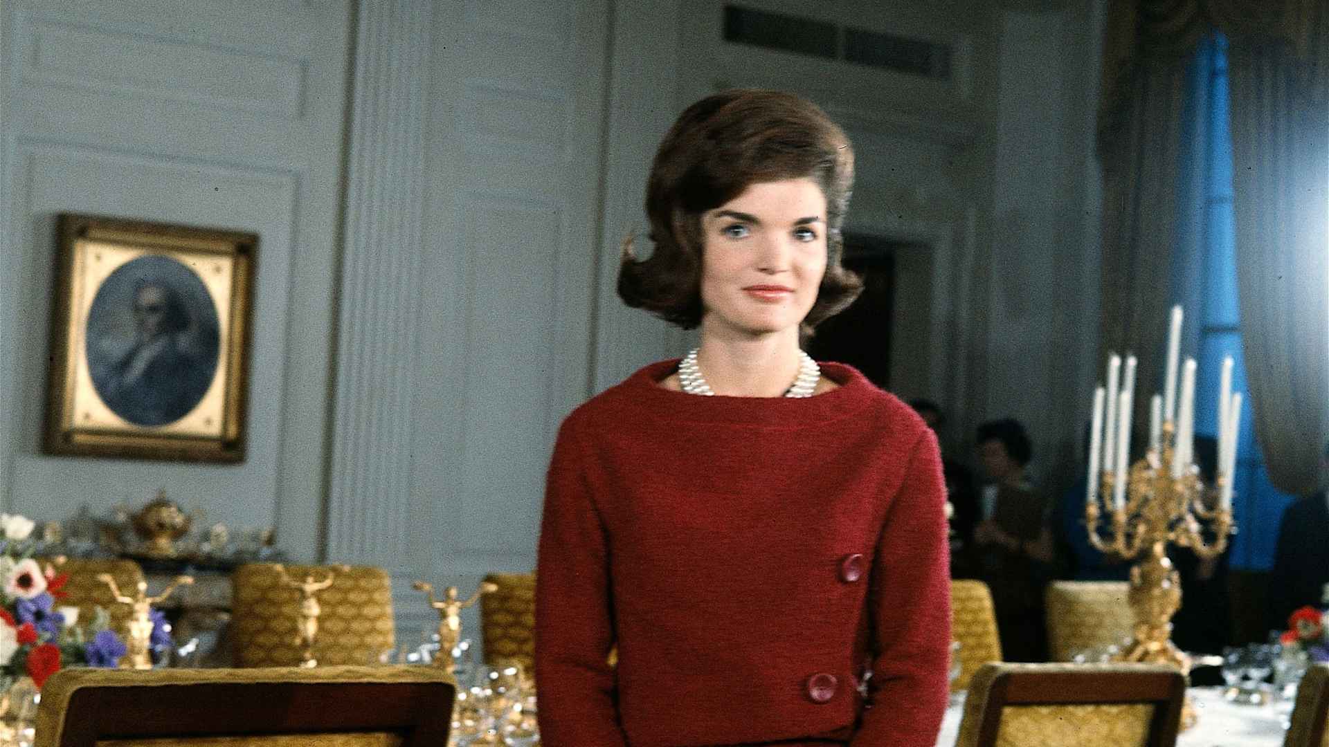 American First Lady Jacqueline Kennedy (1929-1994), in a red dress, stands before a dining room table in the White House during the filming of a CBS News Special program called 'A Tour of the White House with Mrs. John F. Kennedy,' Washington, D.C., January 15, 1962.