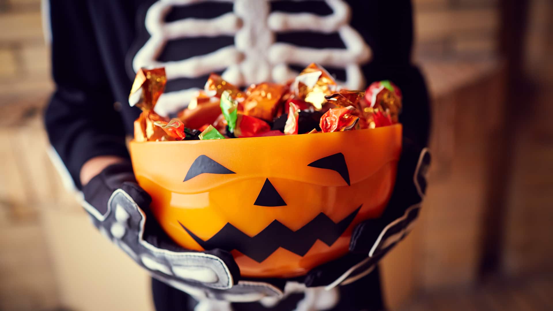 Boy in skeleton costume holding bowl full of halloween candy