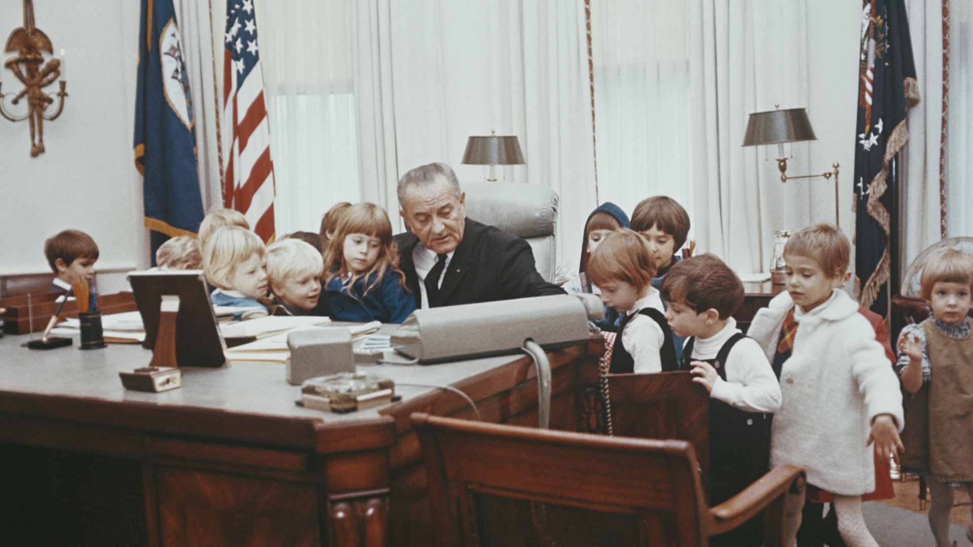 President of the United States, Lyndon B Johnson (1908-1973) pictured sitting at the Johnson desk as he gives a group of young children a tour of the Oval Office in the White House in Washington DC, circa 1967.