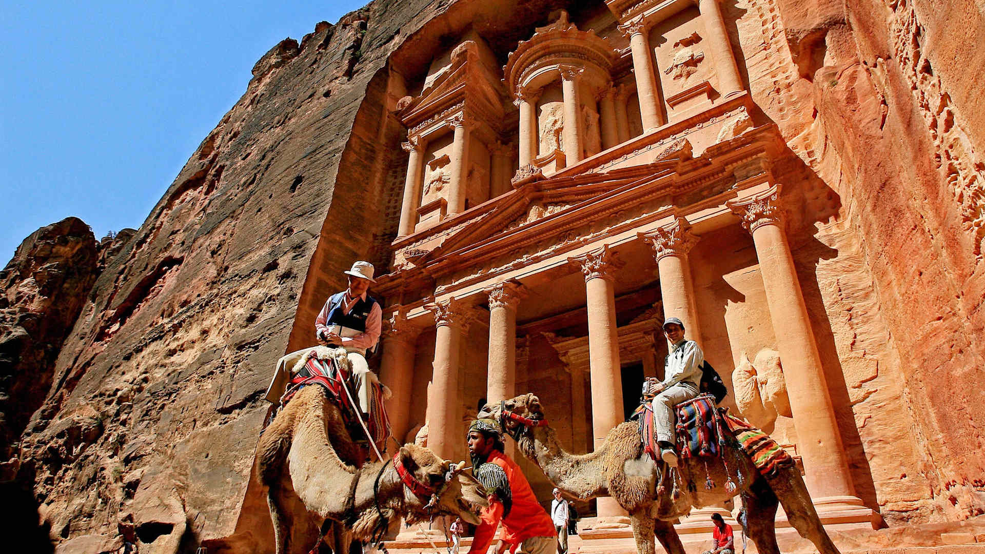 Petra, JORDAN: Tourists ride camels at the ancient ruins of Petra in Jordan, 16 May 2007. Petra is hosting a two-day conference dubbed as "Petra III: Building a Better World" near the site of Jordan's famed Nabataean ruins. The conference is a collaboration between the King Abdullah II Fund for Development and the Elie Wiesel Foundation for Humanity AFP PHOTO/MARWAN NAAMANI (Photo credit should read MARWAN NAAMANI/AFP via Getty Images)
