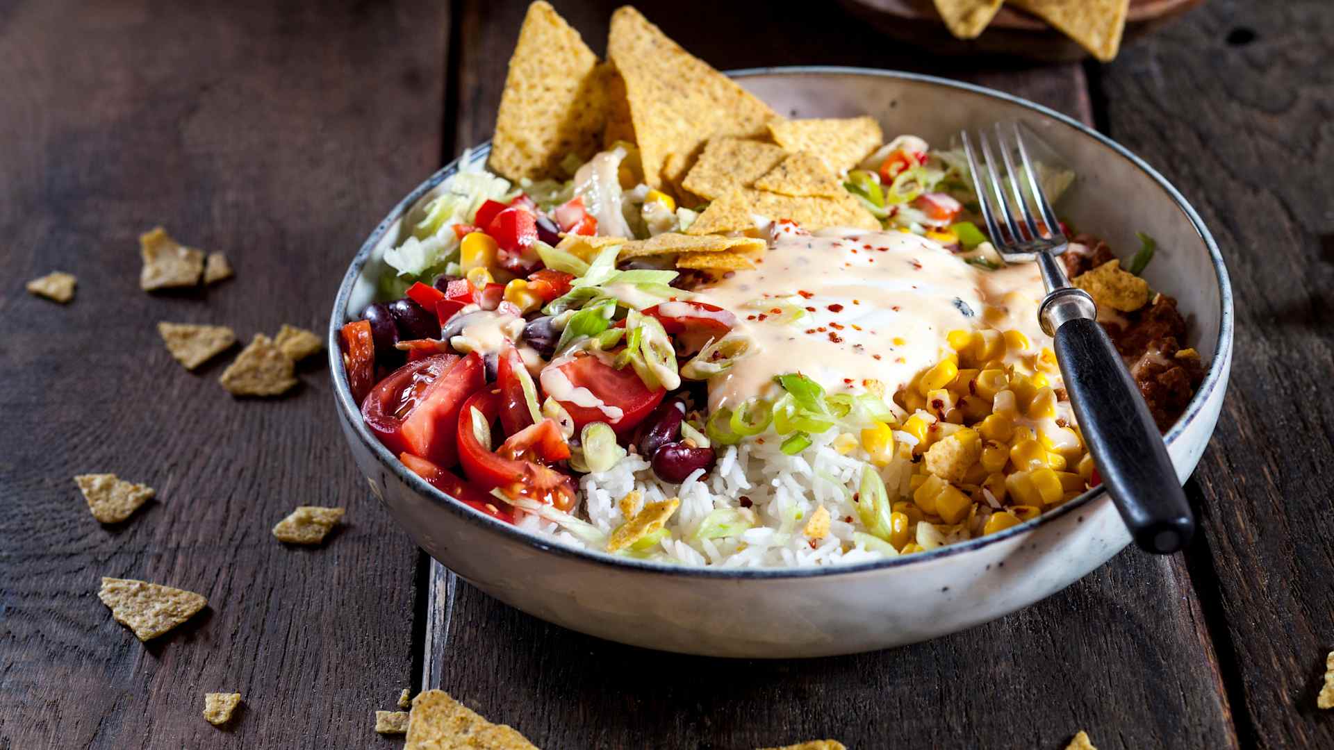 Taco salad bowl with rice, corn, chili con carne, kidney beans, iceberg lettuce, sour cream, nacho chips, tomatoes - stock photo