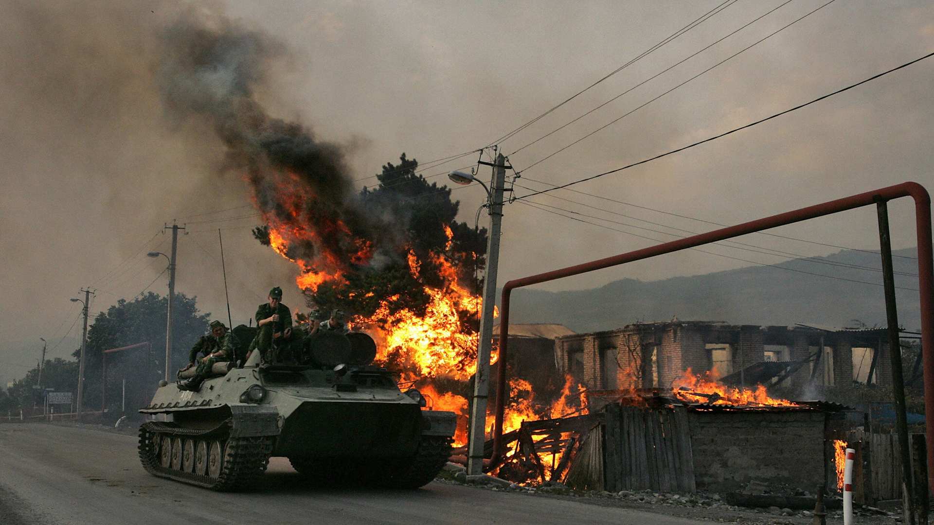 A Russian armored troop-carrier moves with soldiers atop next to a house set on fire by South Ossetian militia on in August, 2008.