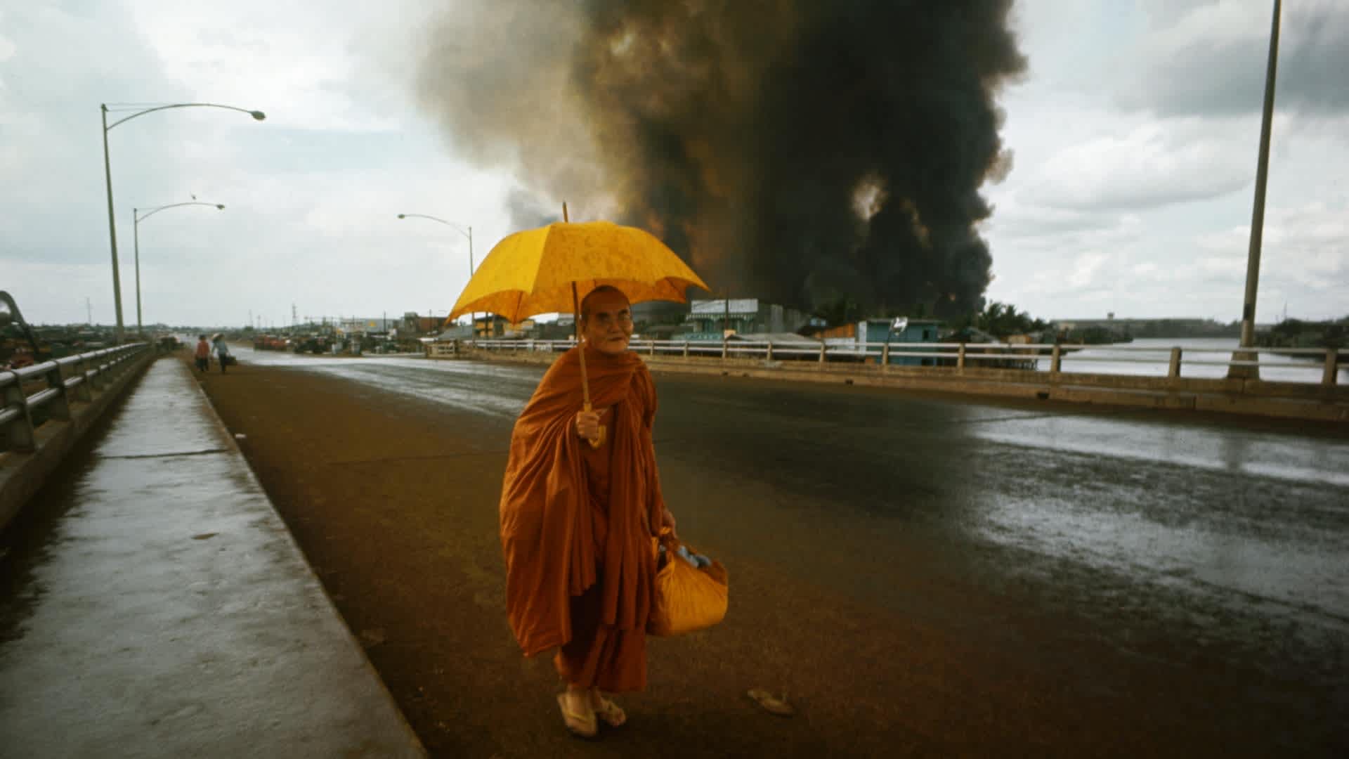 Fires burn behind a Buddhist monk crossing a bridge on the first day of the Tet Offensive