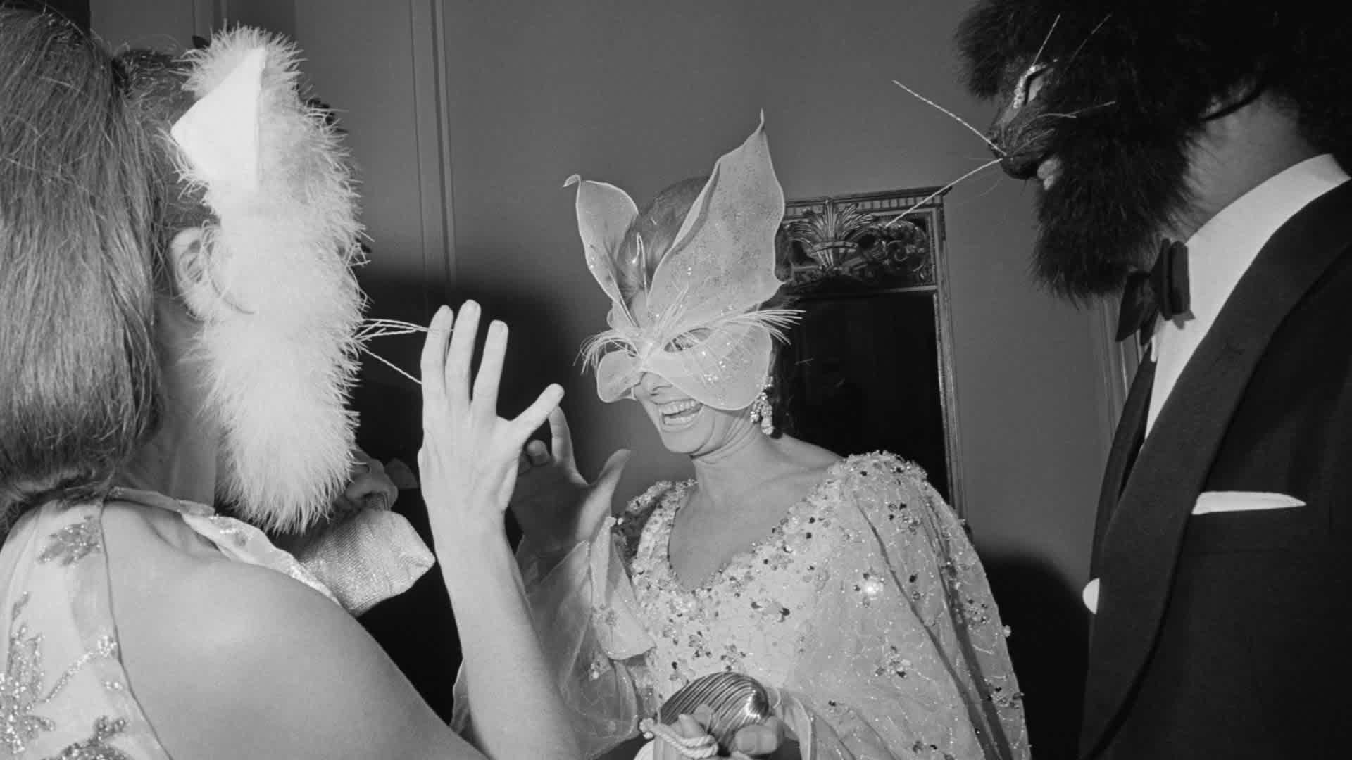 Vogue Editor Francoise Langlade (left) and Oscar de la Renta (right) in cat masks speaking with Anne McDonnell, wife of Henry Ford, in a butterfly mask.