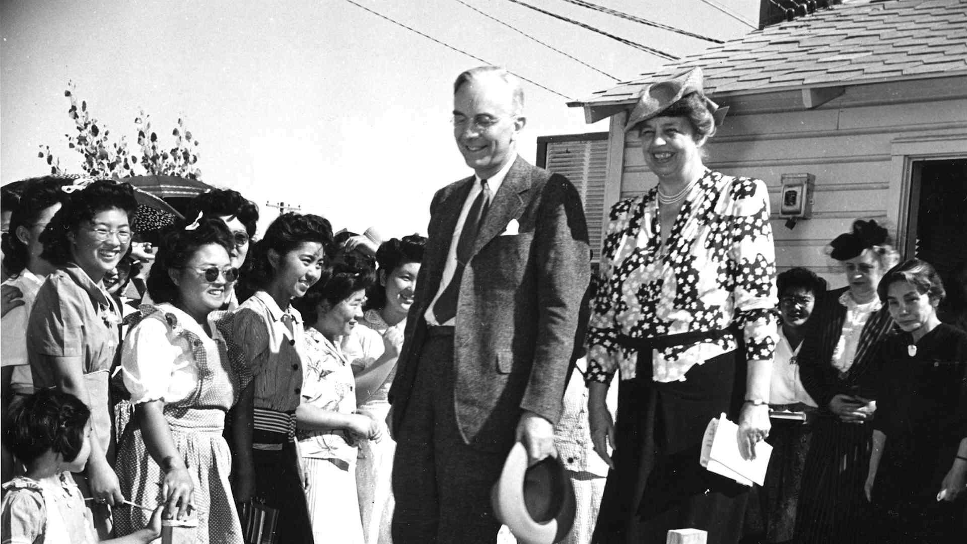 First Lady Eleanor Roosevelt smiles at a group of Japanese American women in the sunshine as she tours an internment camp