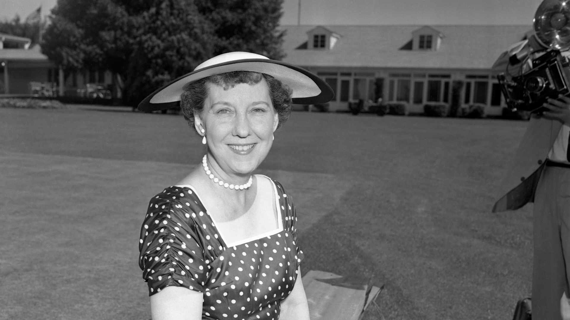First Lady Mamie Eisenhower wears her Easter outfit consisting of a Sally Victor hat of white straw with a wide edging of navy, a deep navy blue dress with white polka dots and a blue faille duster.