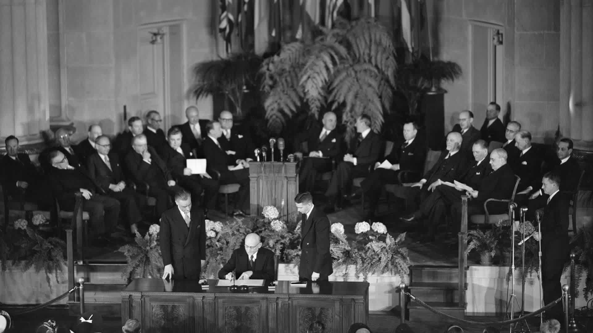 Signing Nato Agreement(Original Caption) 4/4/1949- Washington, DC- French Foreign Minister Robert Schuman signs the North Atlantic Treaty. At the tabe in foreground are (L-R): France's Amb to the U.S. Henry Bonnet; Schuman; John W. Foley, State Dept treaty adv. In front row on platform are (L-R): Foreign Ministers Ernest Bevin, GB; Halvard Lange, Nry; Josef Bech, Lux; Bjarni Benediktsson, Icld; Gustav Rasmussen, Dnmk; Paul-Henry Spaak, Blgm; President Truman.