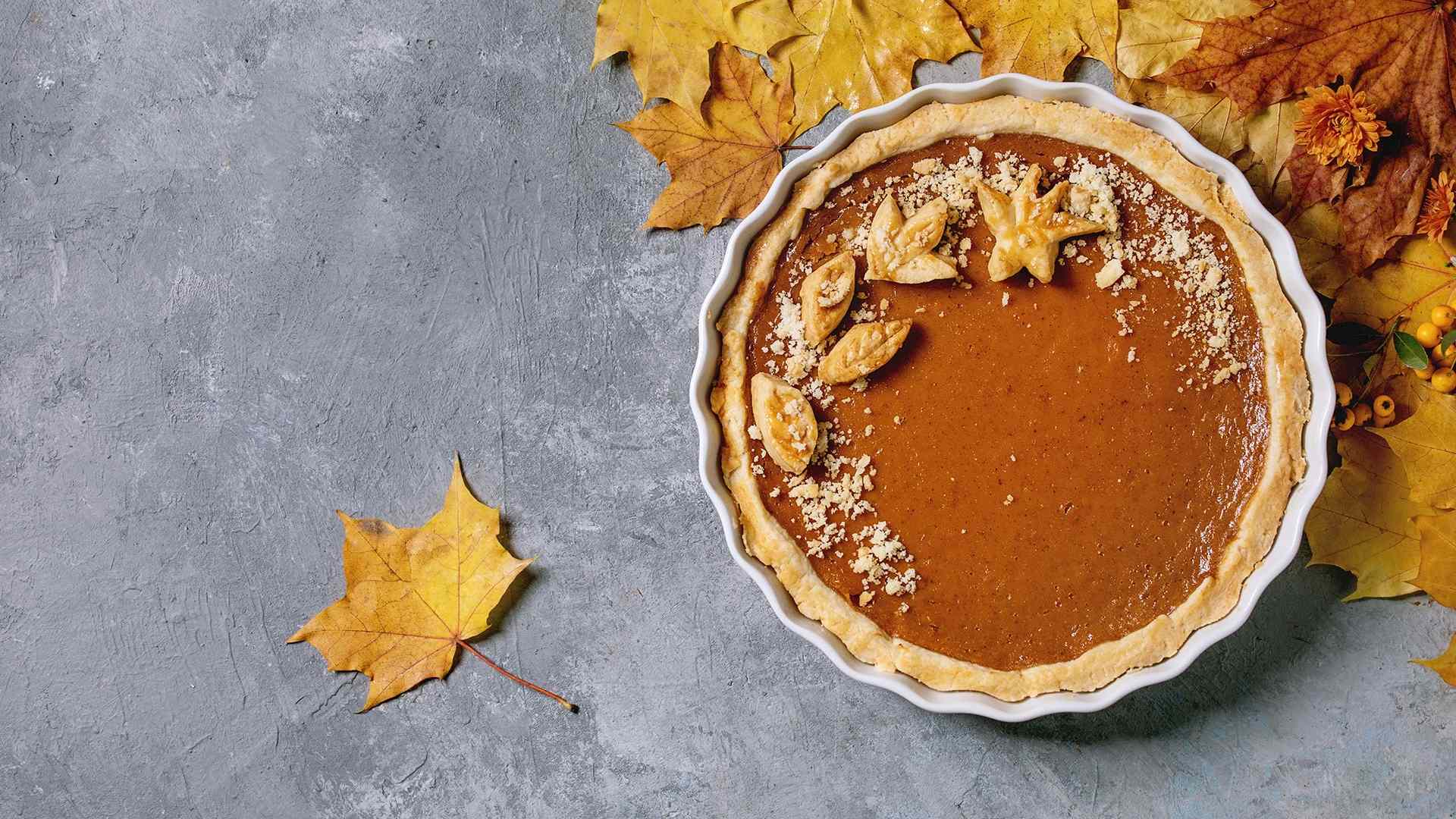 Traditional homemade autumn pumpkin pie for Thanksgiving or Halloween dinner served in ceramic dish with yellow autumn leaves over grey texture background. Flat lay, space. (Photo by: Natasha Breen/REDA&CO/Universal Images Group via Getty Images)