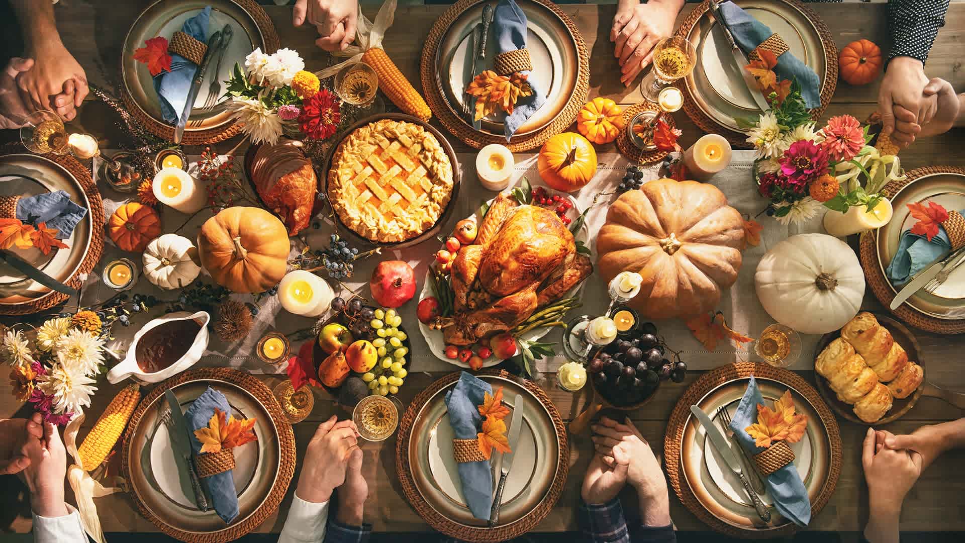 A group of friends or family members hold hands around a Thanksgiving