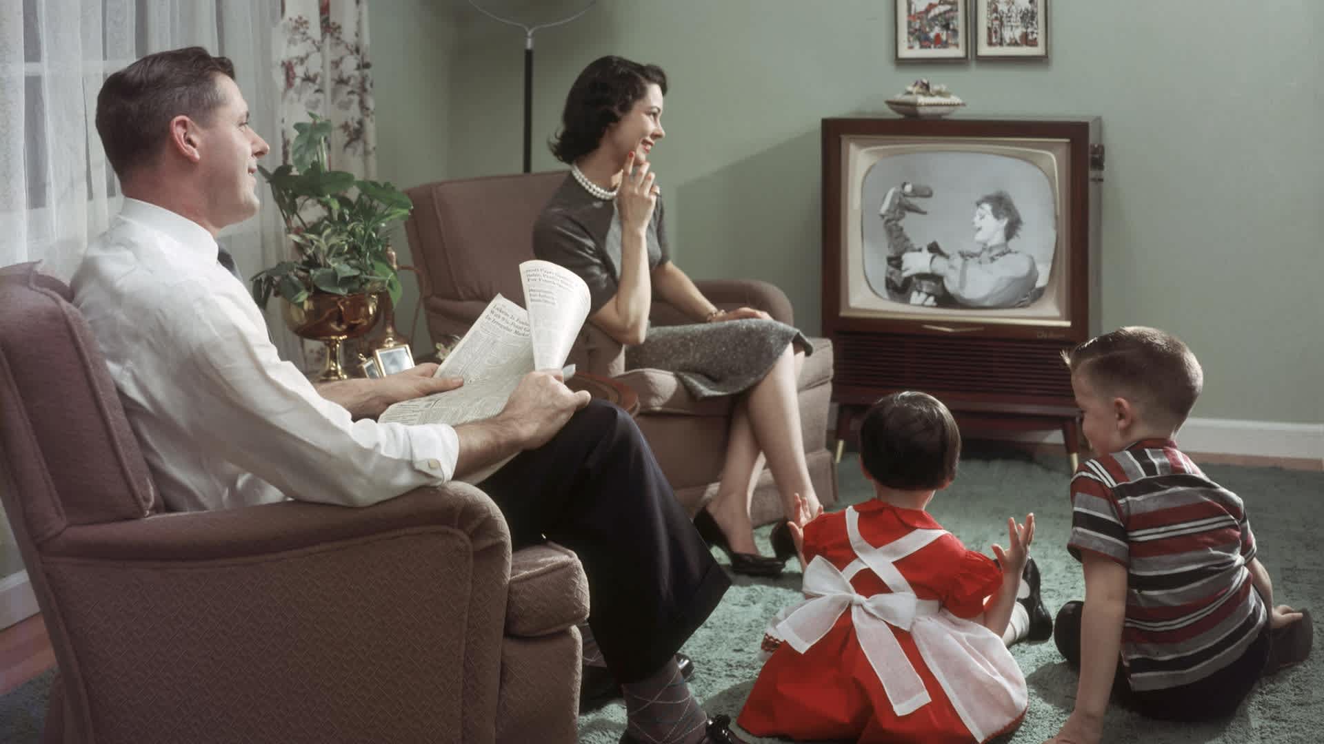 TV Time TogetherA happy family cheerfully sits in their living room and watches a televisied clown and puppet show, 1957. The father holds an newspaper open to the financial section in his hands. (Photo by Lambert/Getty Images)