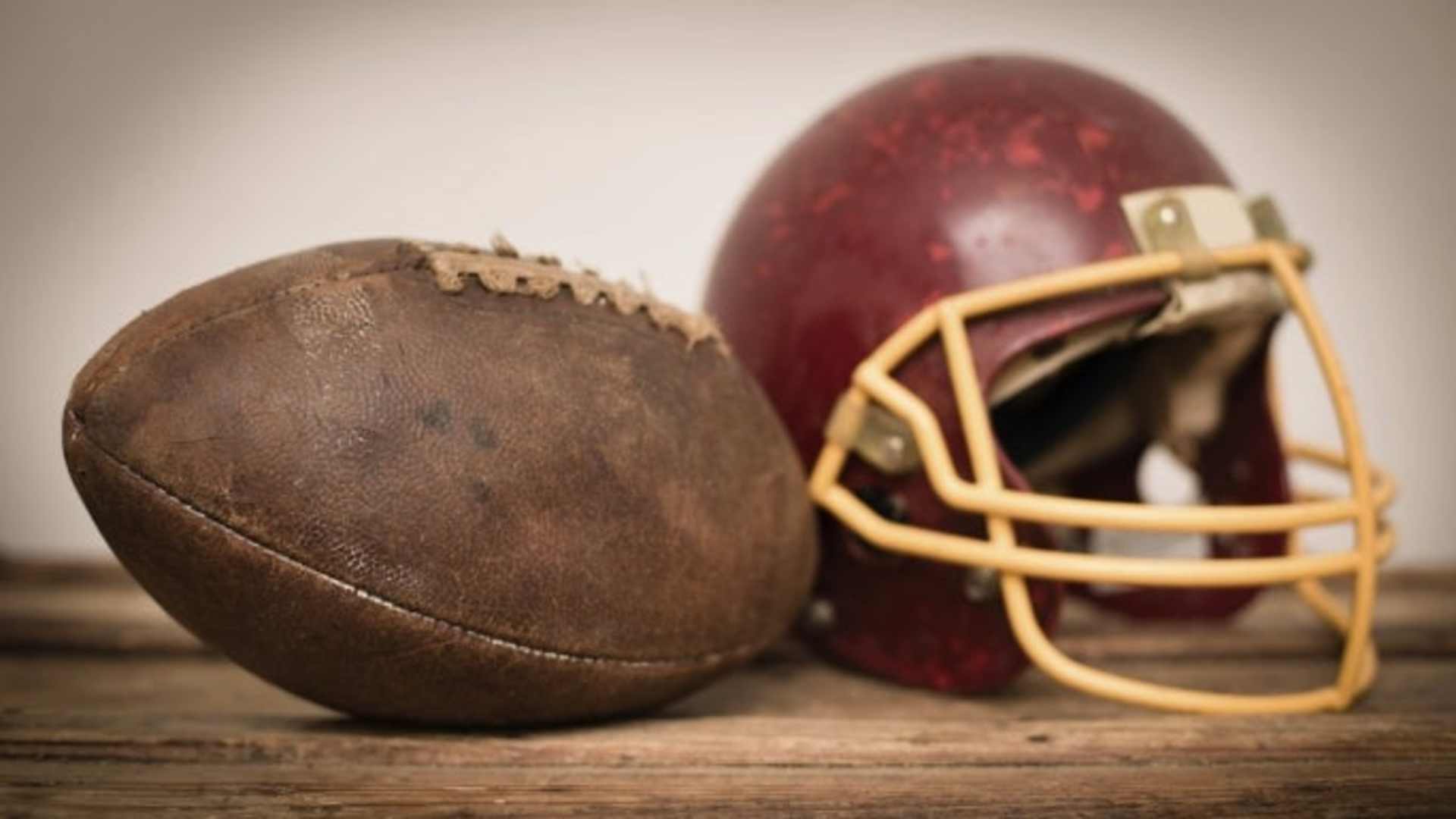 Close up, color image of a vintage football helmet and football, sitting on wood. Some desaturation and grain added for vintage feel.