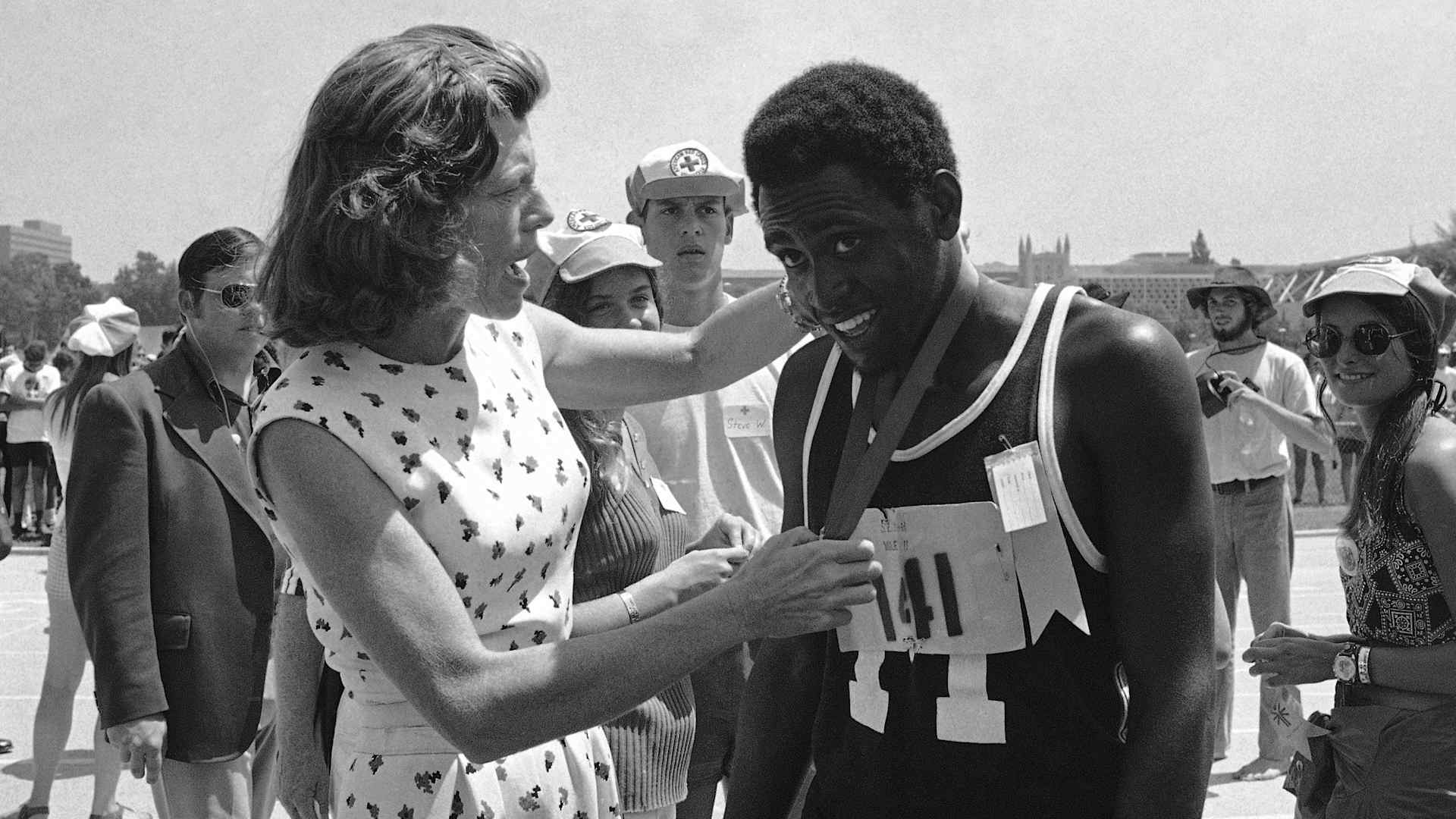 Eunice Kennedy Shriver, founder of the Special Olympics, hanging a gold medal around  18-year-old Adonis Brown of Baltimore after winning the mile run in 5 minutes, 12 seconds in the 1972 International Special Olympics in Los Angeles.