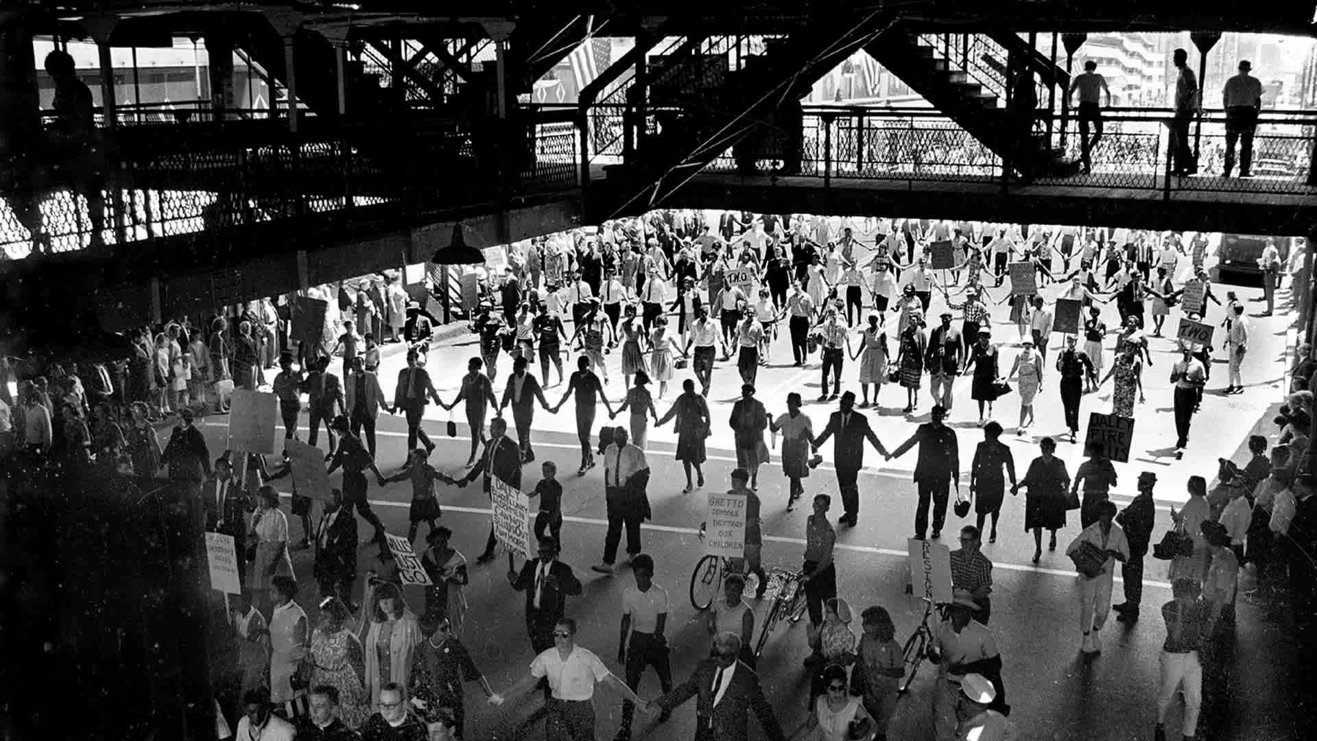 Demonstrators marching under the Chicago "L" (elevated railroad) during a protest calling for the firing of School Superintendent Benjamin Willis by Mayor Daley over the delays in integrating Chicago schools during the 1960s. (Credit: Robert Abbott Sengstacke/Getty Images)