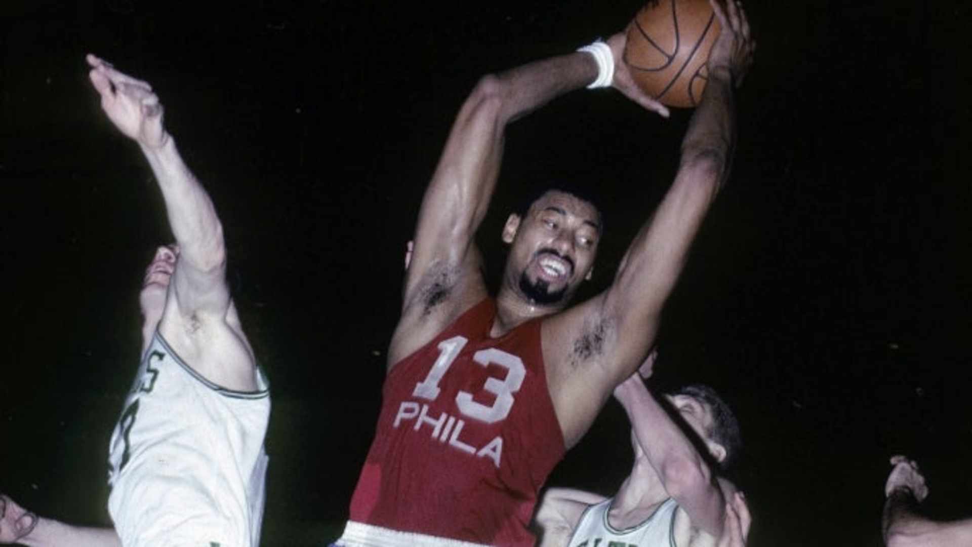 Wilt Chamberlain of the Philadelphia 76ers pulls down a rebound against the Boston Celtics during a mid-1960s game at Boston Garden. (Credit: Focus on Sport/Getty Images)