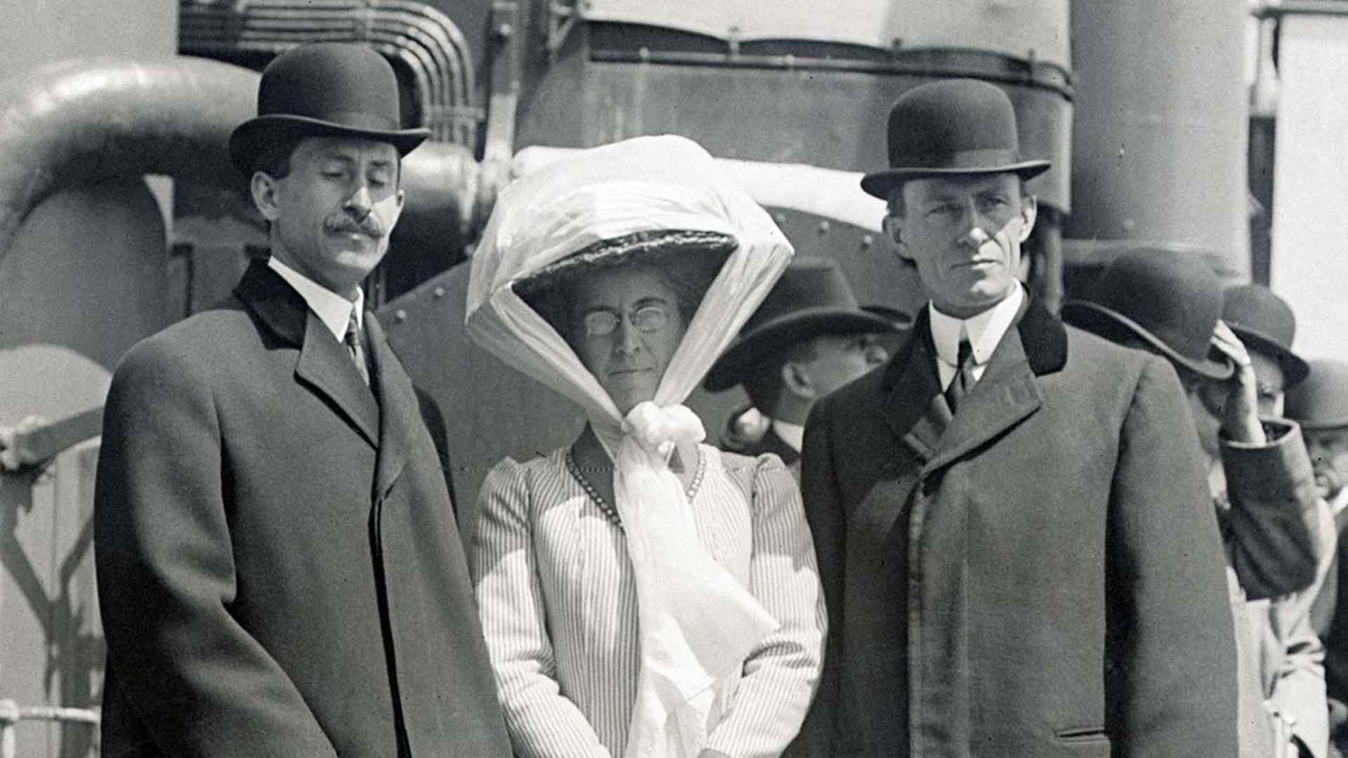 Full-length portrait of inventors Orville Wright (L) and Wilbur Wright (R) standing with their sister Katherine Wright (center) on the deck of a ship, circa 1910.
