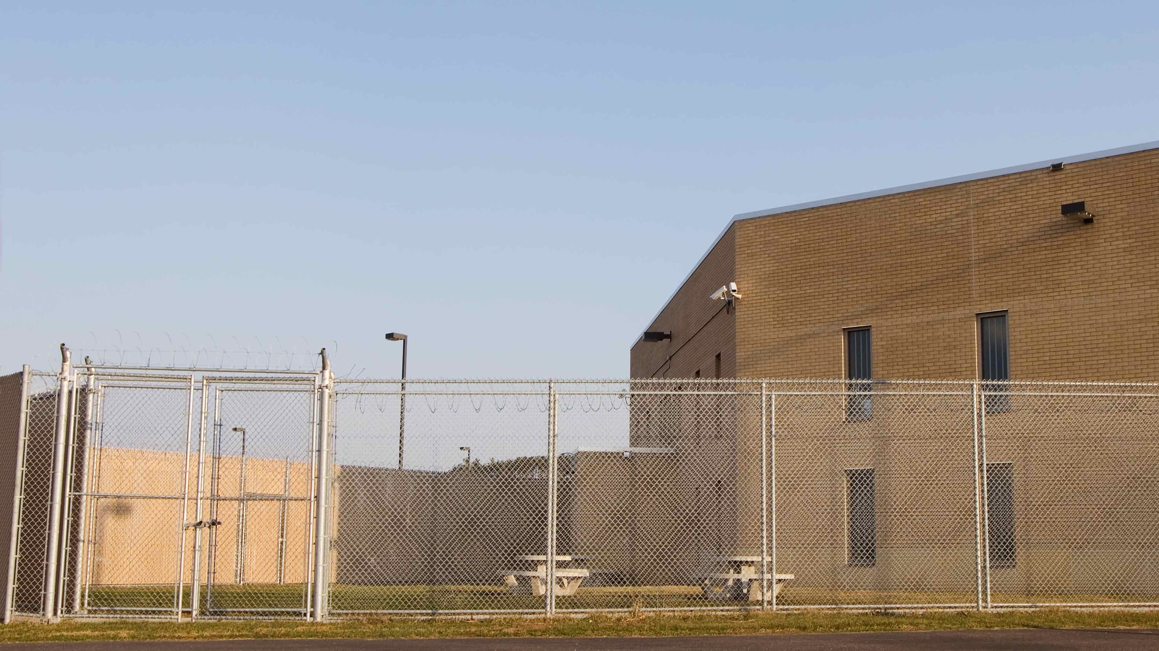 An empty fenced prison yard with prison behind